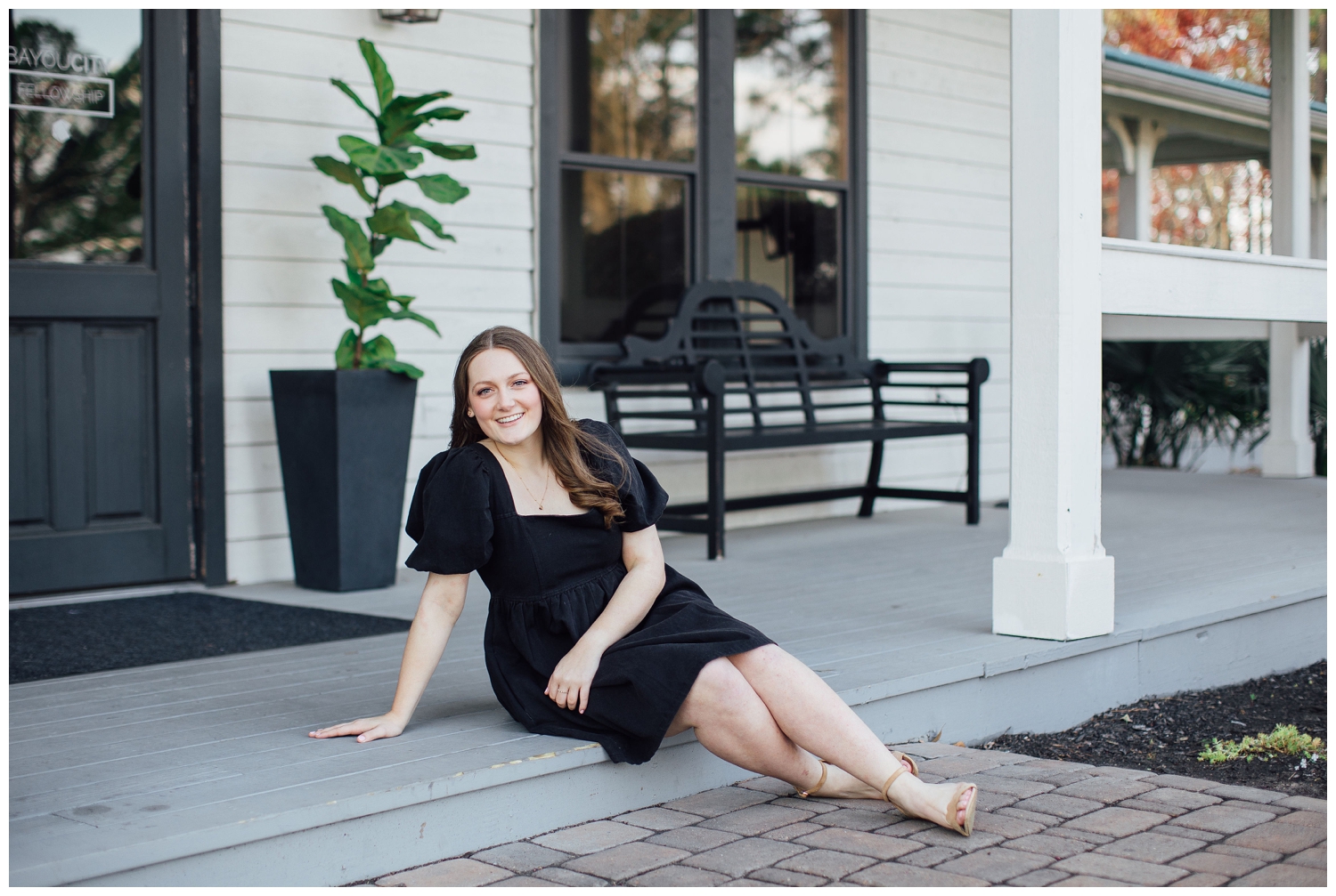 high school senior wearing black dress sitting in front of white building Cypress senior photographer at Cy-Hope