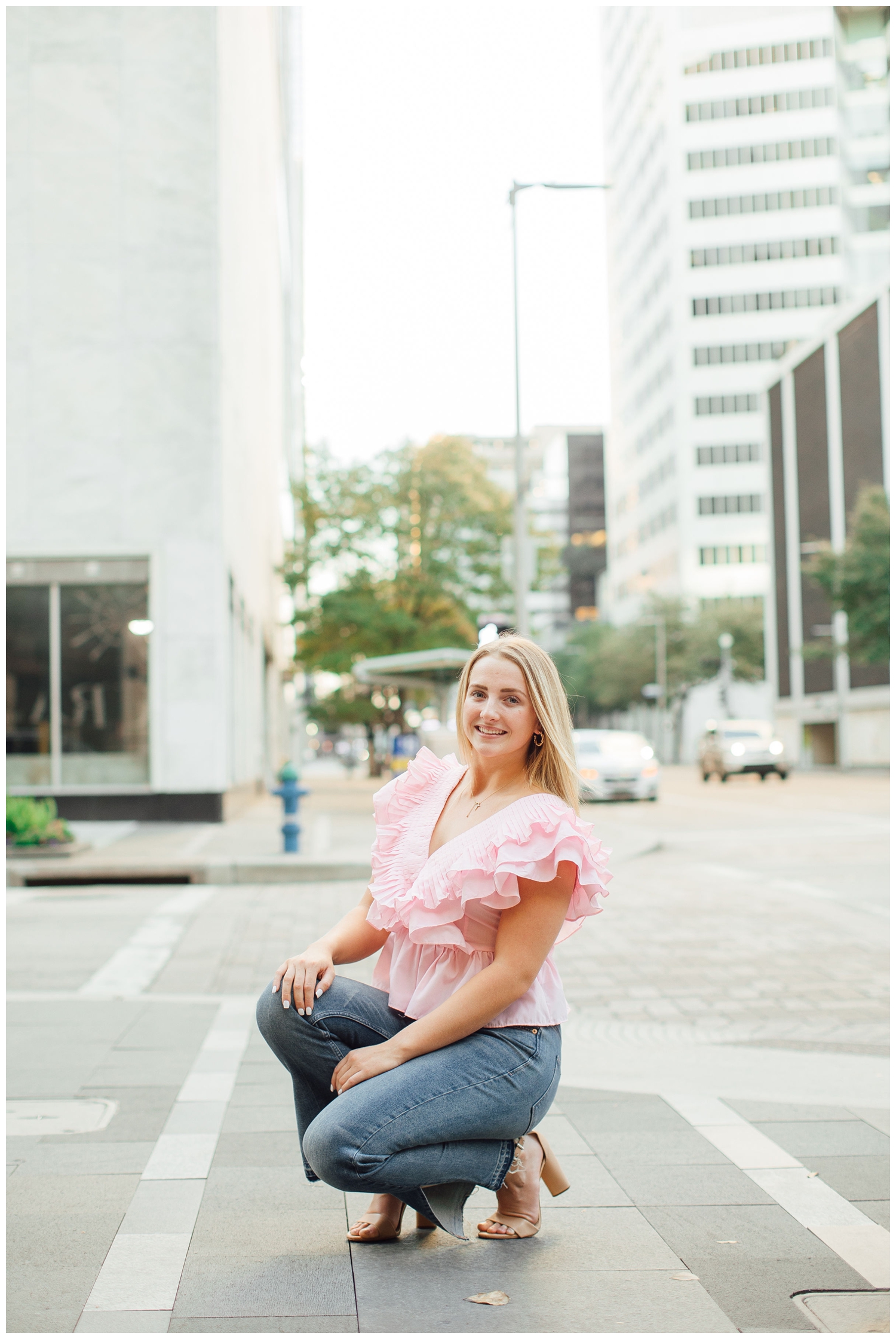 high school senior girl in pink blouse and jeans squatting on urban city streets Houston downtown