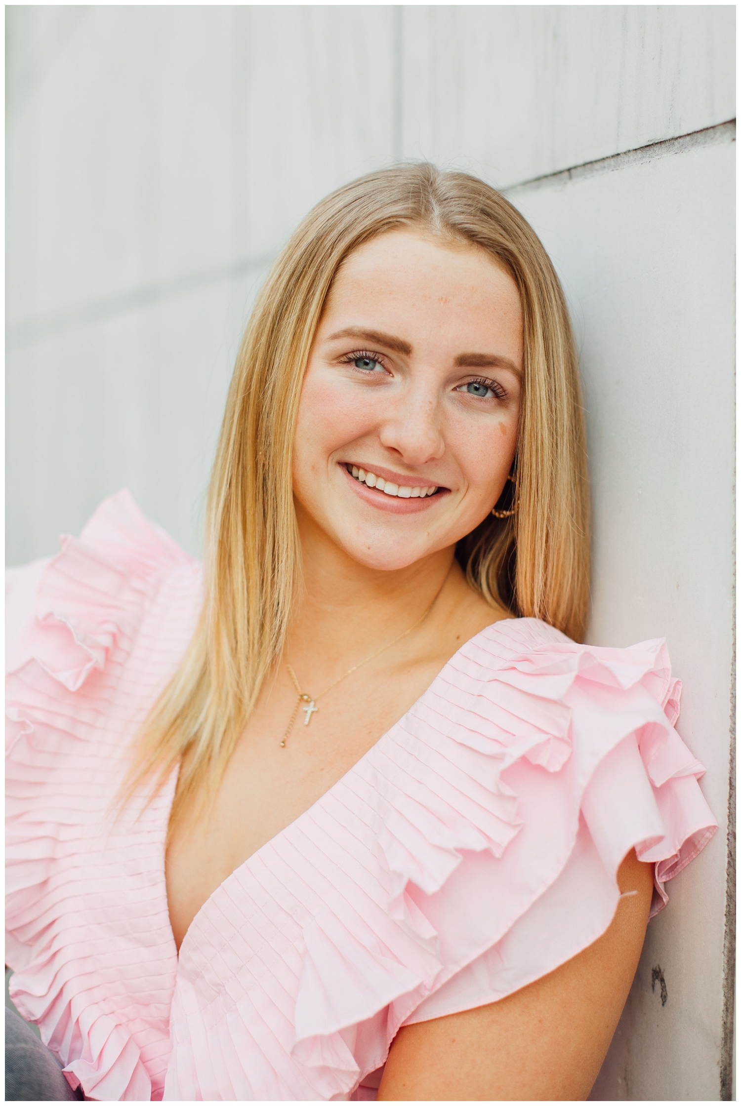 girl in pink blouse leaning against white wall smiling for urban senior photos Houston
