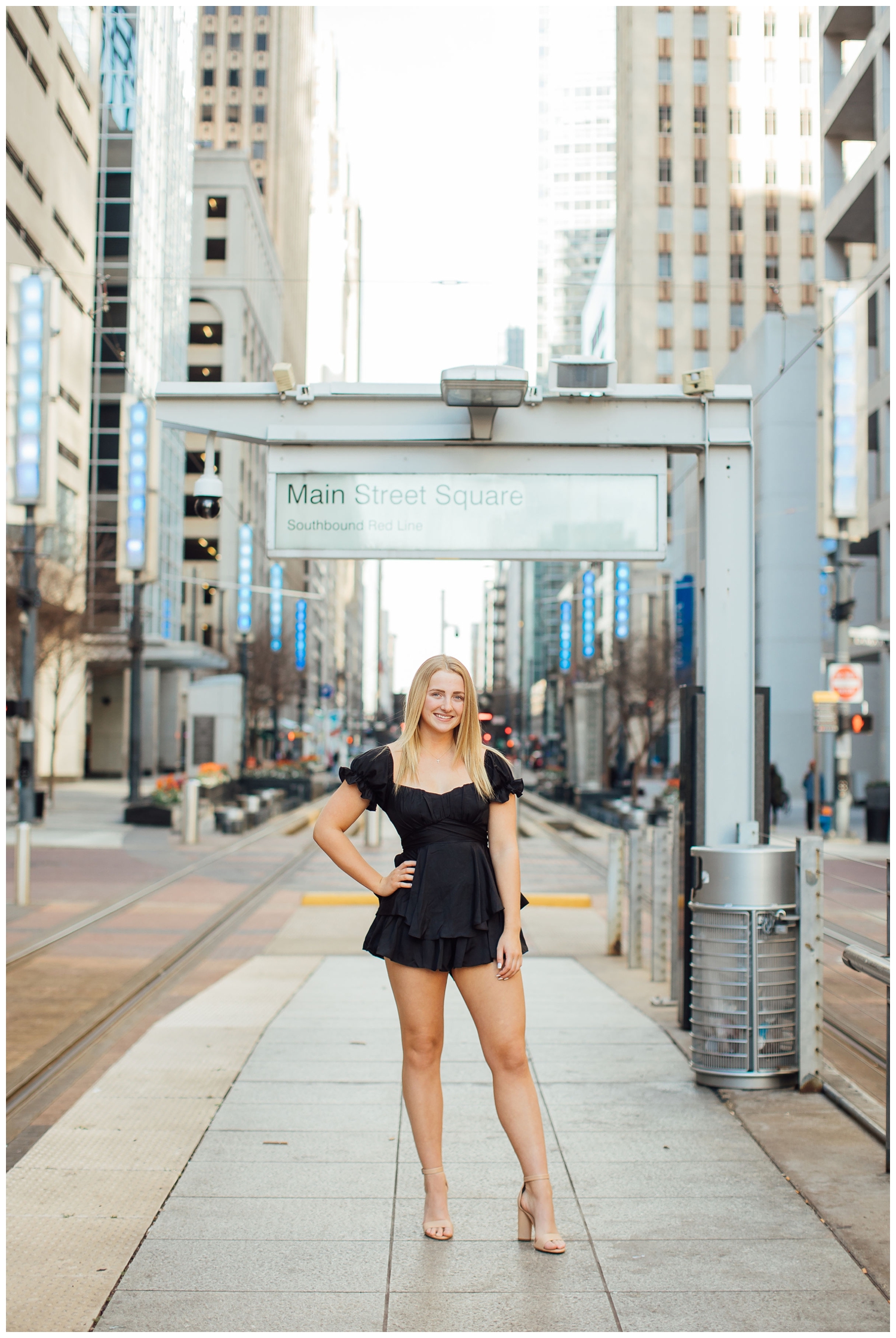 girl with hands on hip in black dress standing in front of Metro Rail urban senior photos Houston downtown Main Street