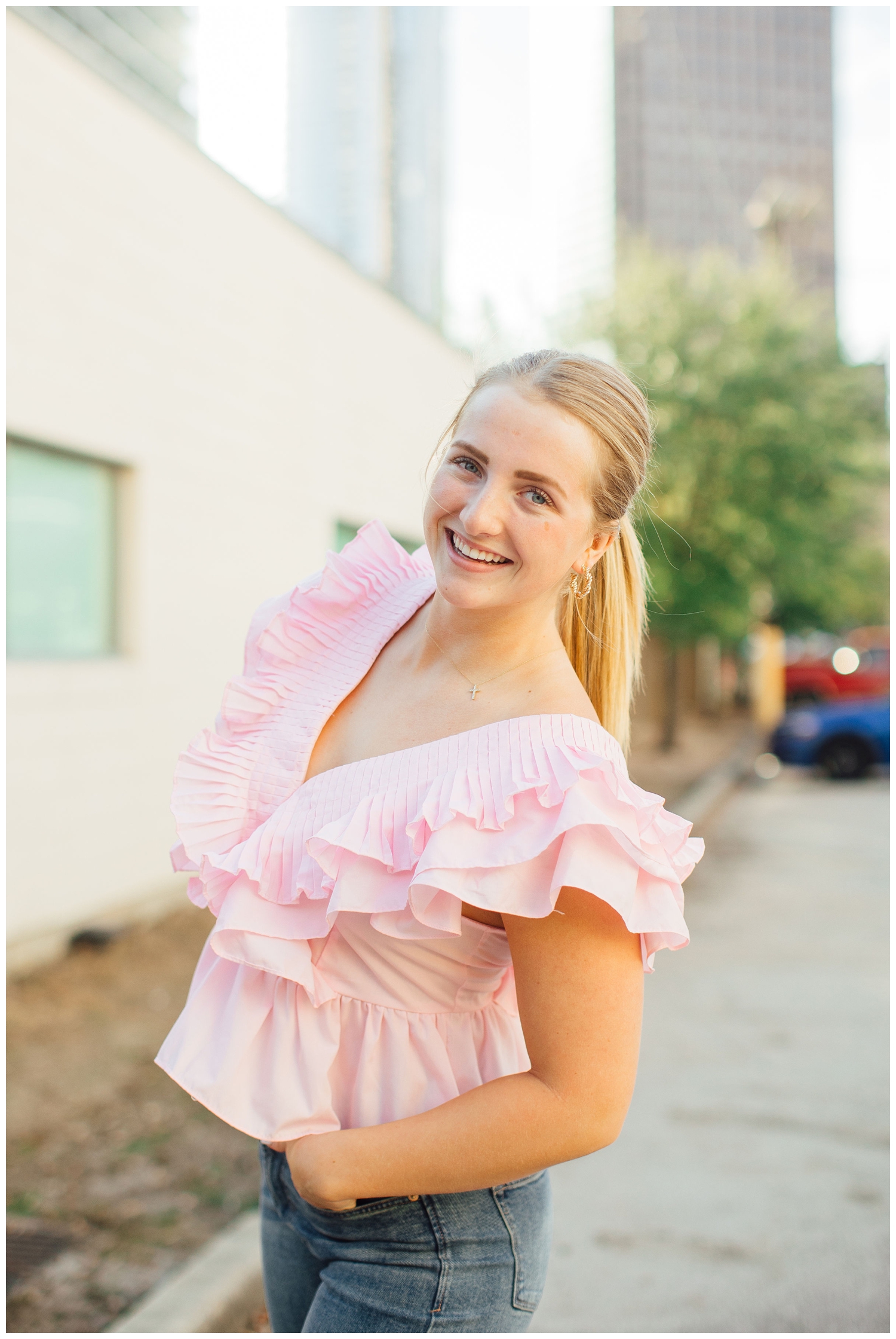 high school senior in pink blouse leaning into camera in downtown Houston