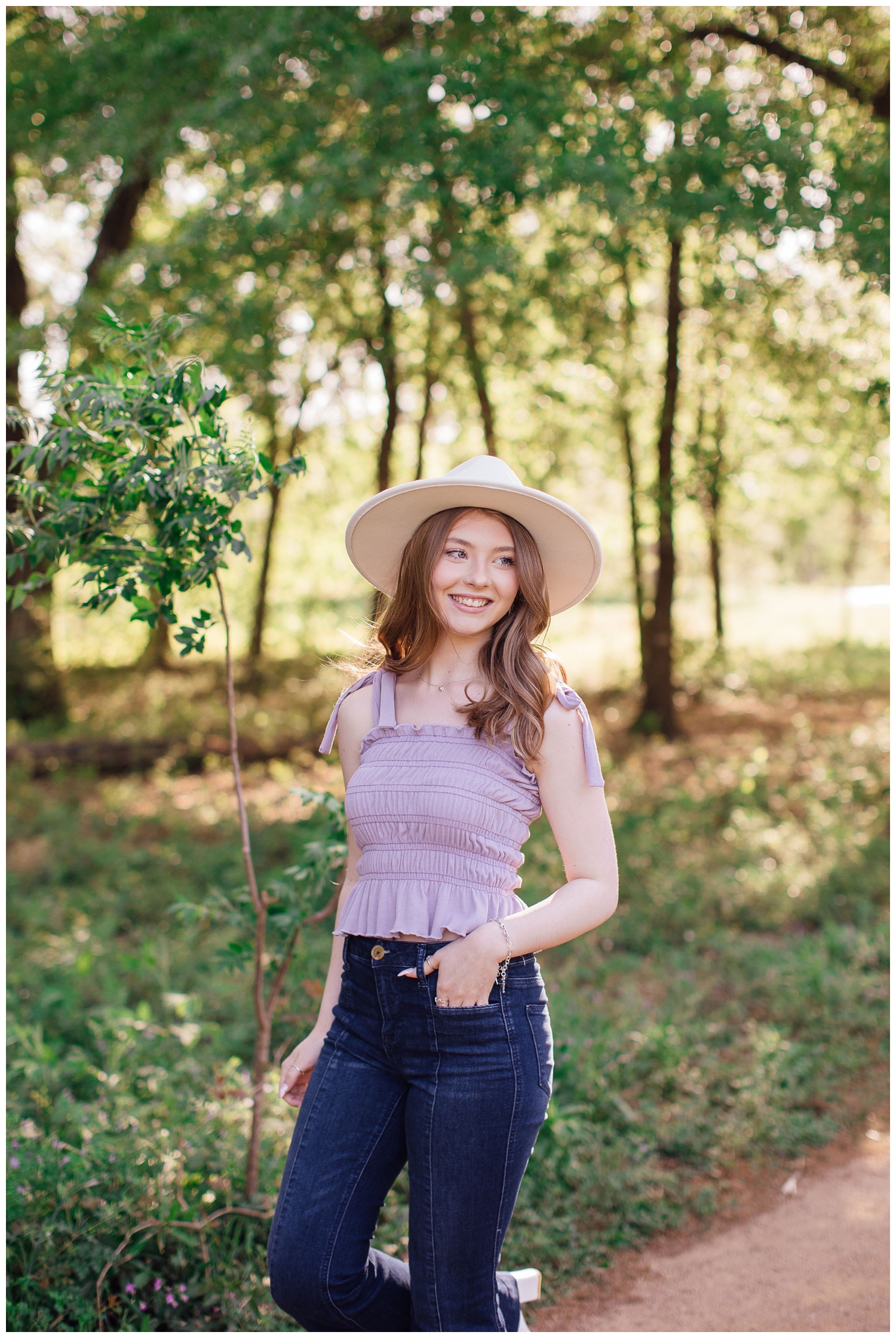 senior girl with hand in denim pocket wearing white brimmed hat outdoors in a field