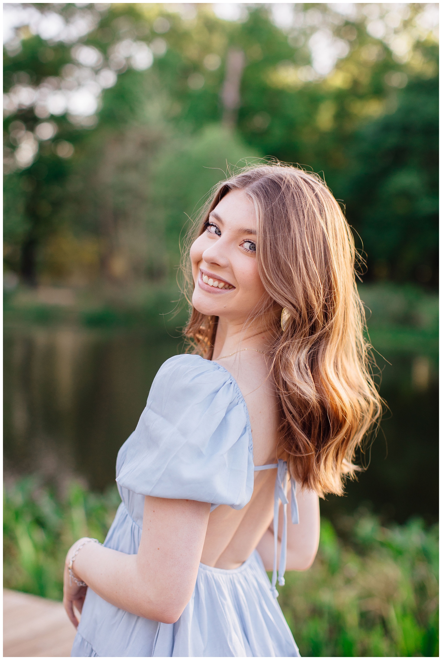 senior girl smiling over shoulder looking at camera standing by a pond