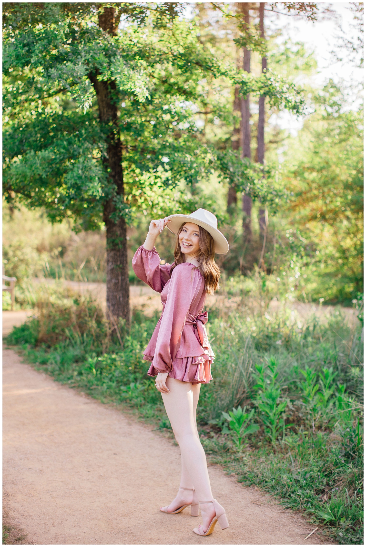 girl standing on pathway at Houston Arboretum holding her hat on head