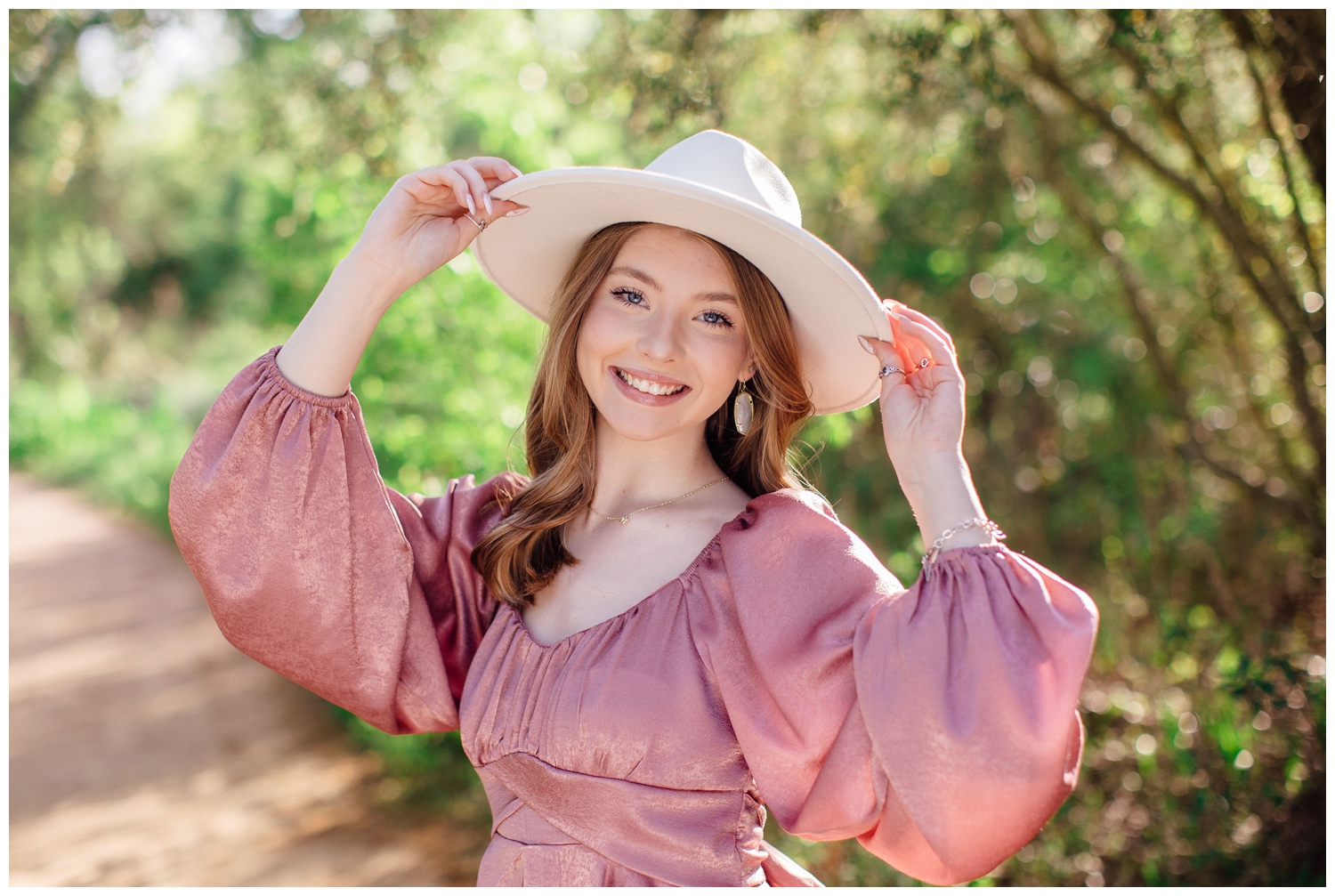 senior girl in mauve dress with both hands on her white cowboy hat