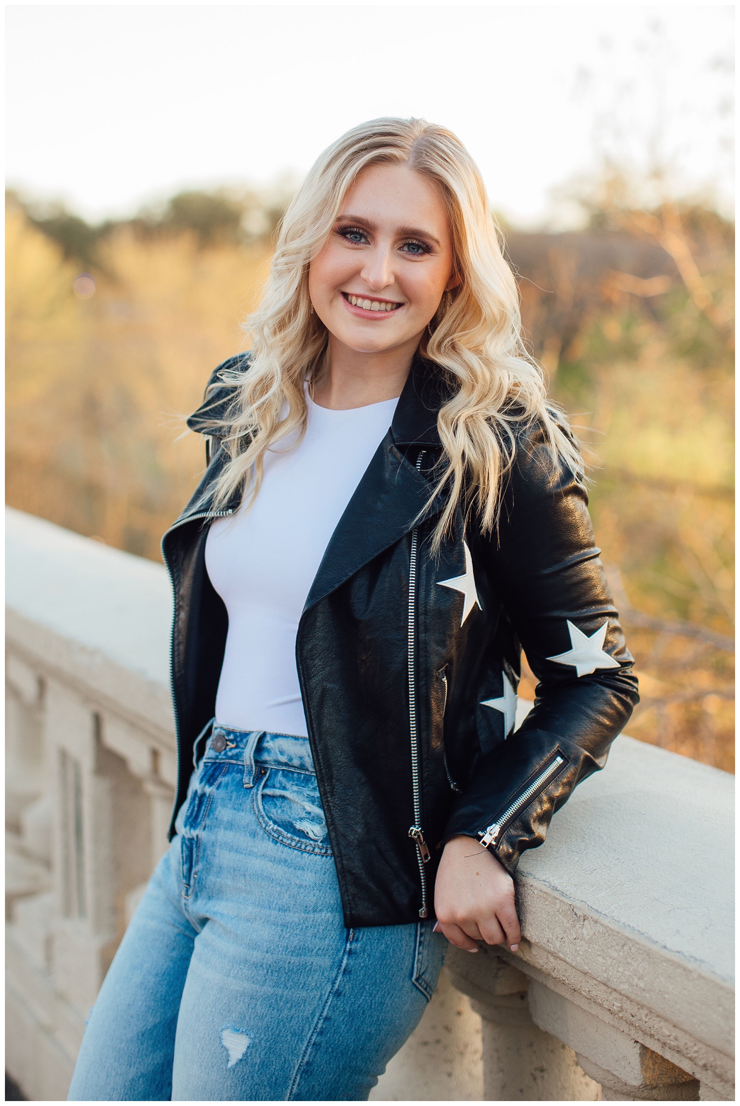 girl wearing black jacket with stars and jeans standing on Sabine Street Bridge for senior pictures Houston Texas
