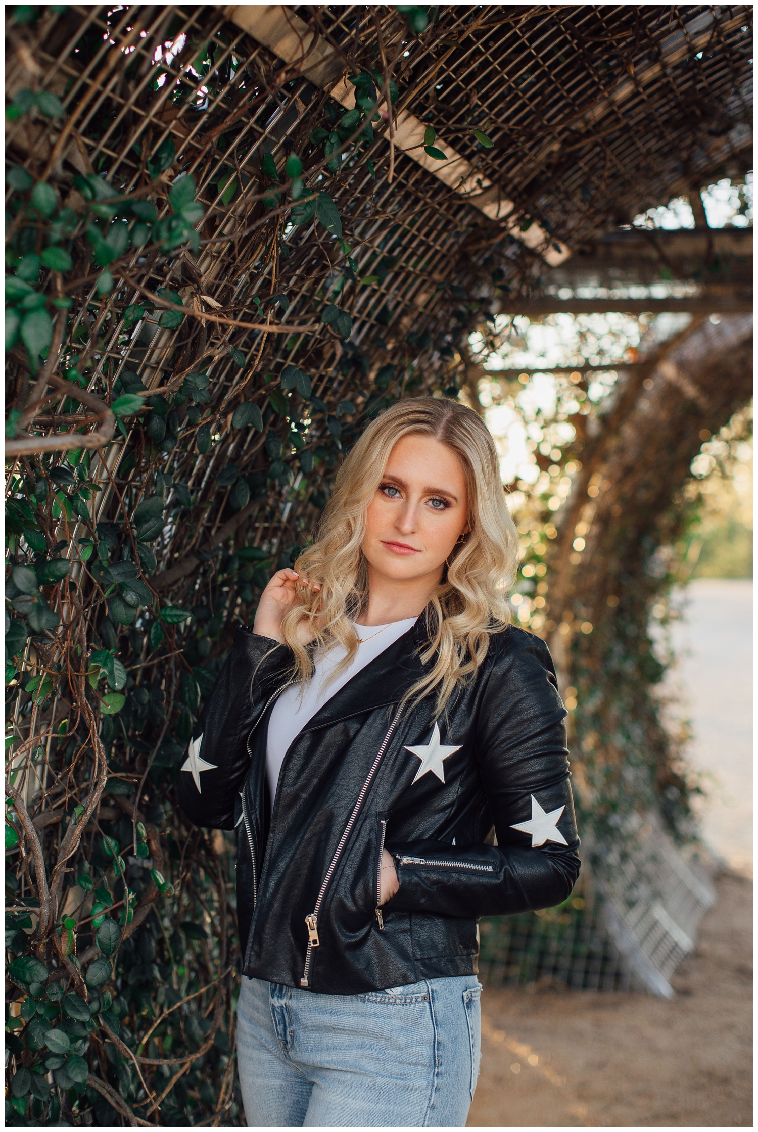 girl in black jacket with stars standing by garden arch at Sabine Street for senior pictures Houston