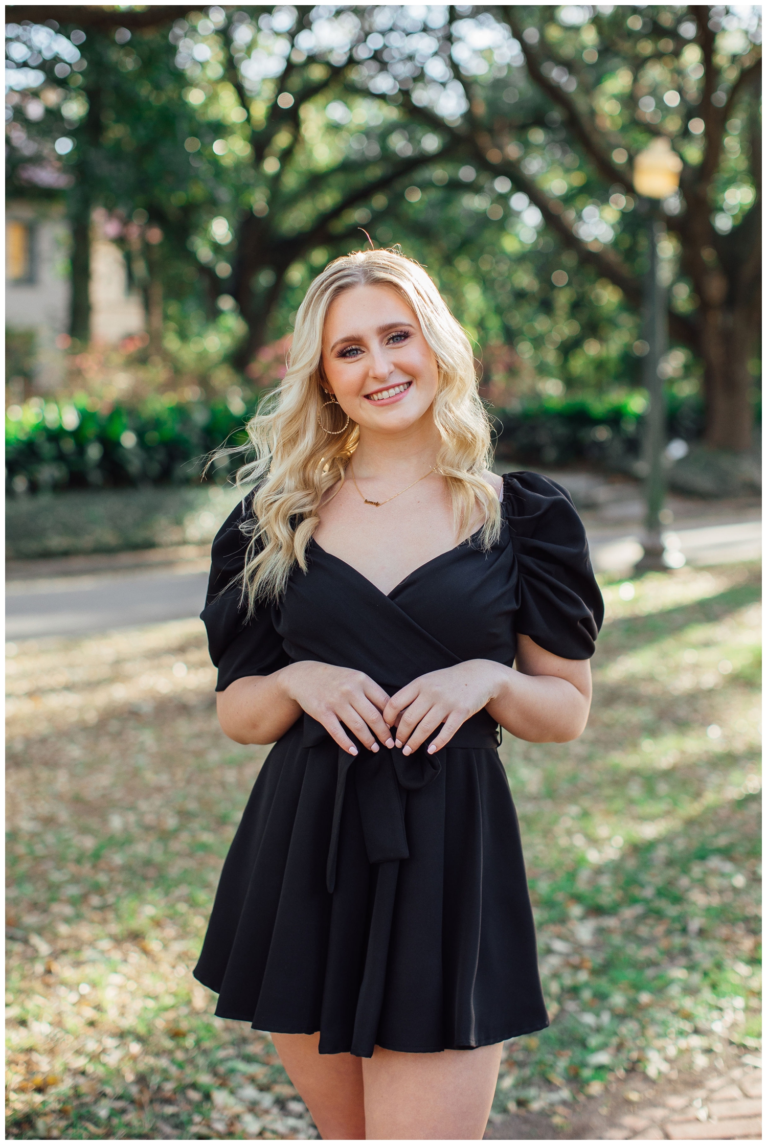 high school senior girl in black dress with hands touching in front of her body standing outdoors Houston