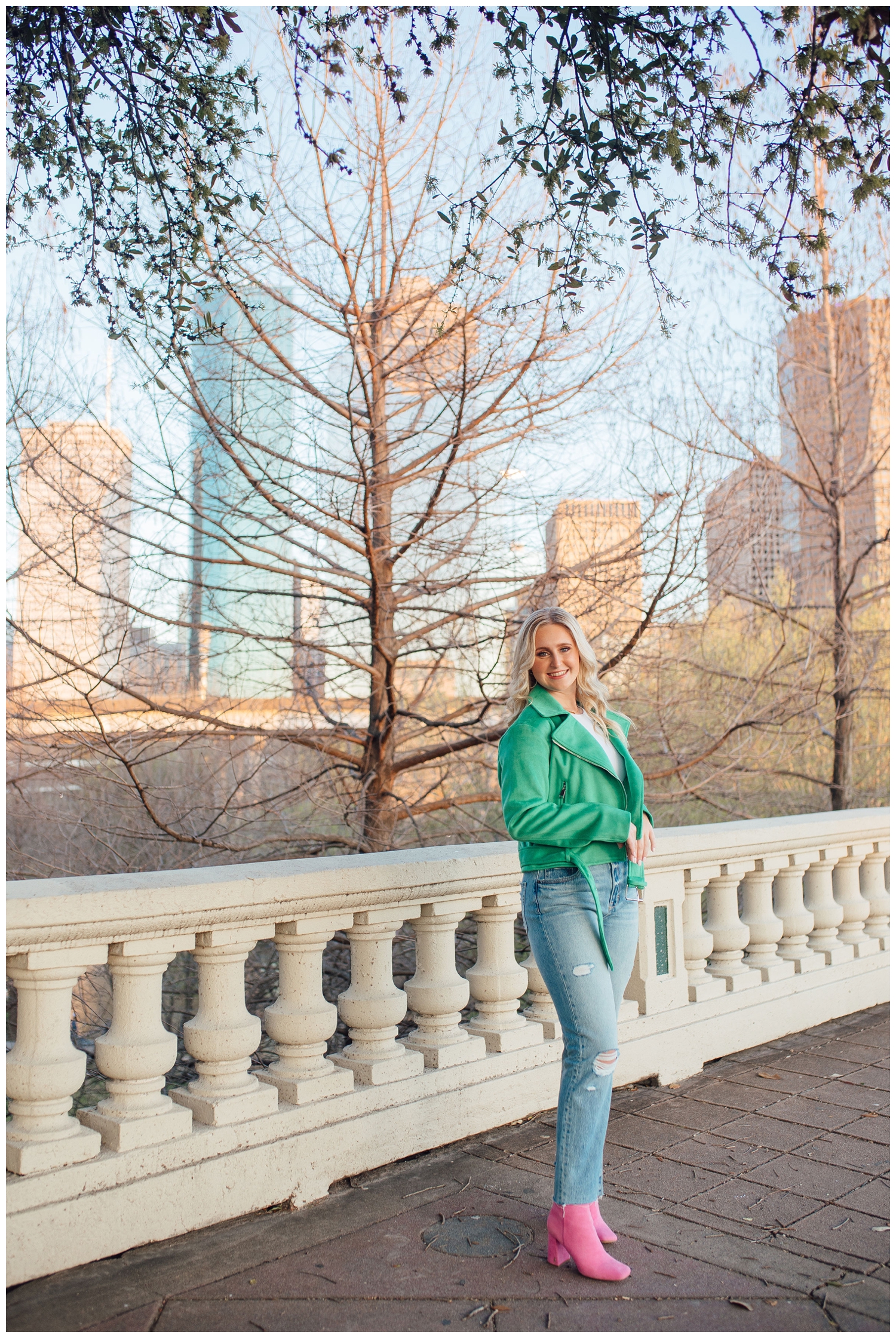 high school senior girl in green jacket and pink boots standing on Sabine Street Bridge Houston skyline