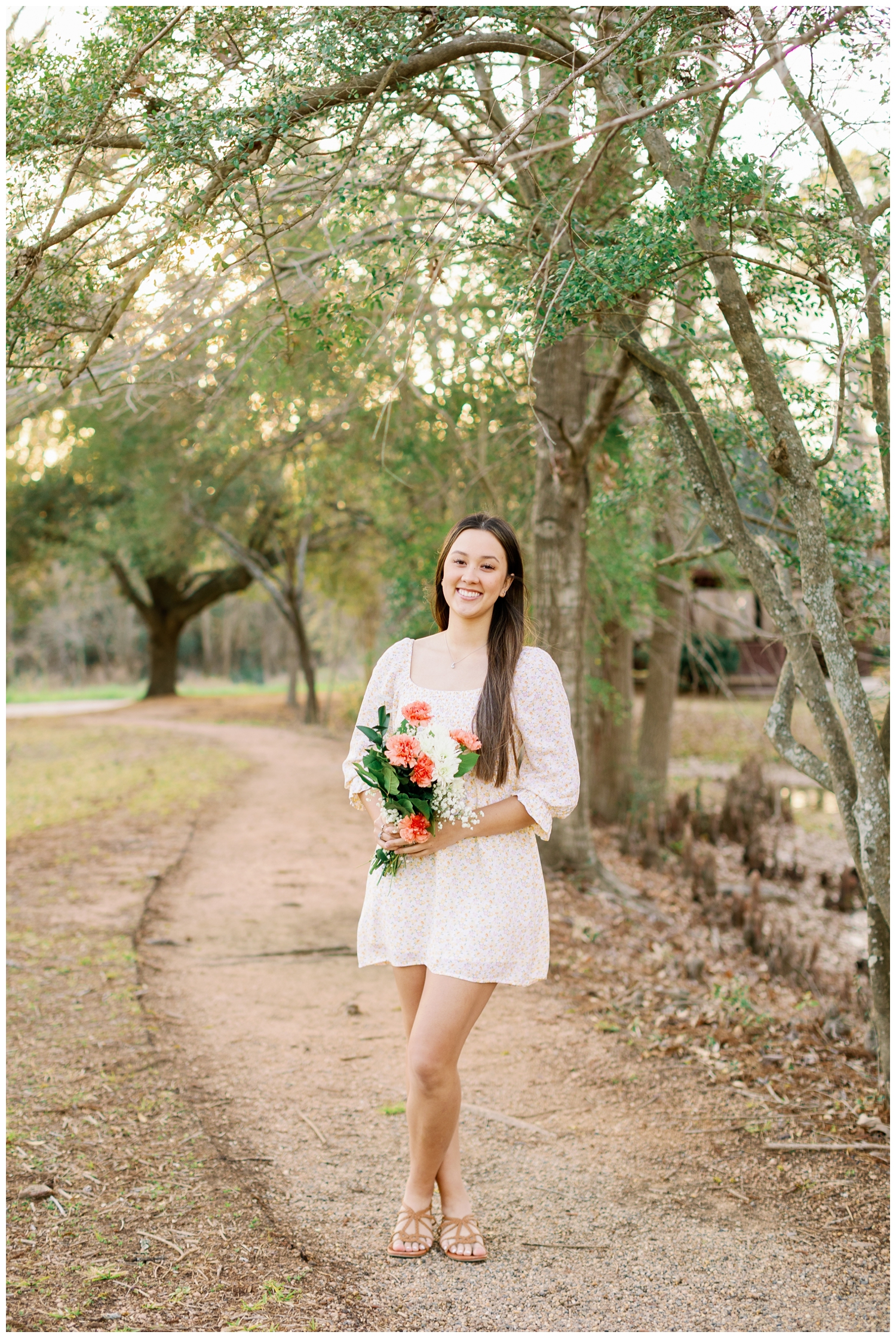 girl in white dress standing on pathway at Cy-Hope holding flowers for spring picnic senior pictures