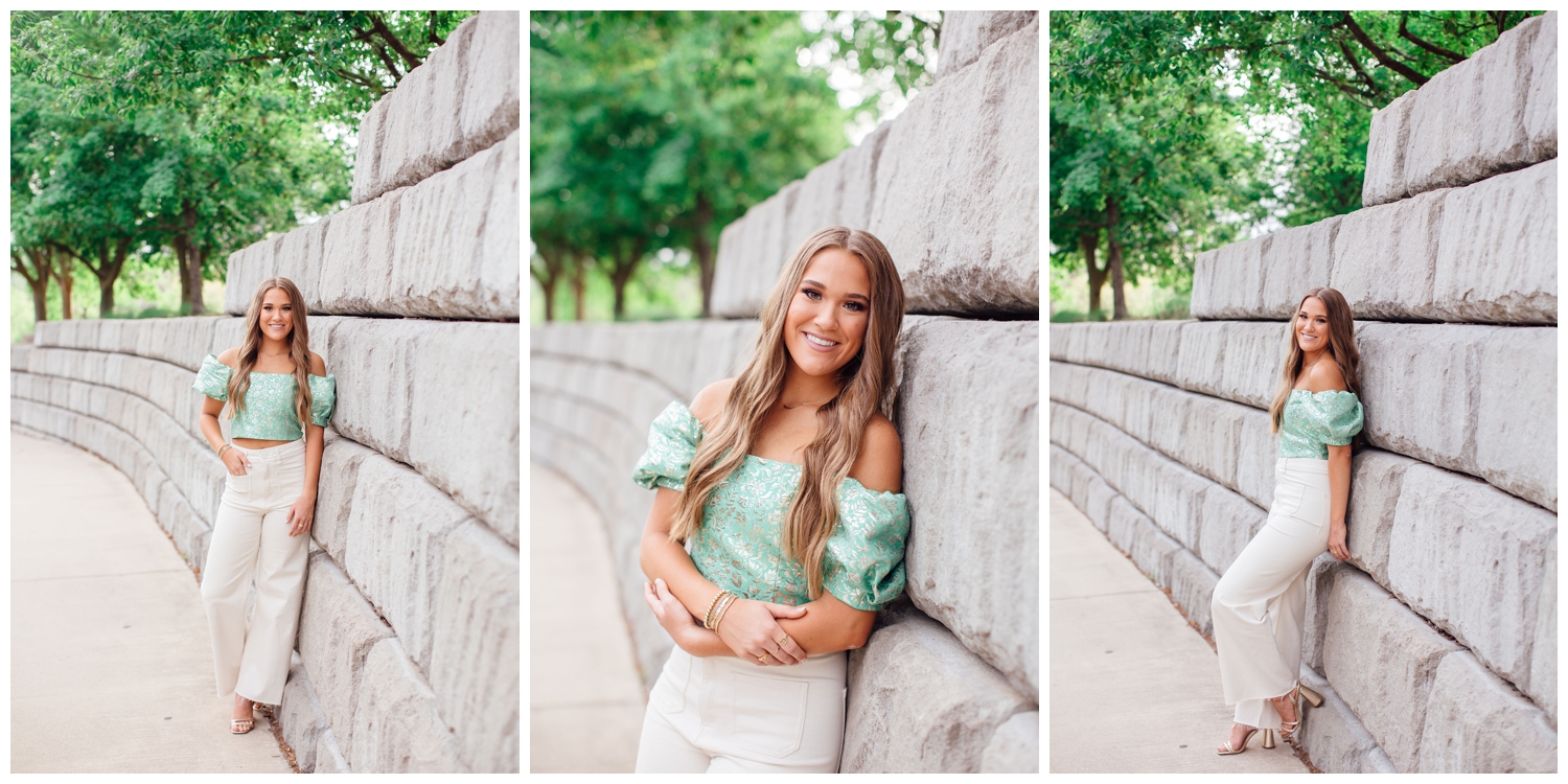 senior girl leaning against gray wall in Buffalo Bayou Houston in green shirt and white pants