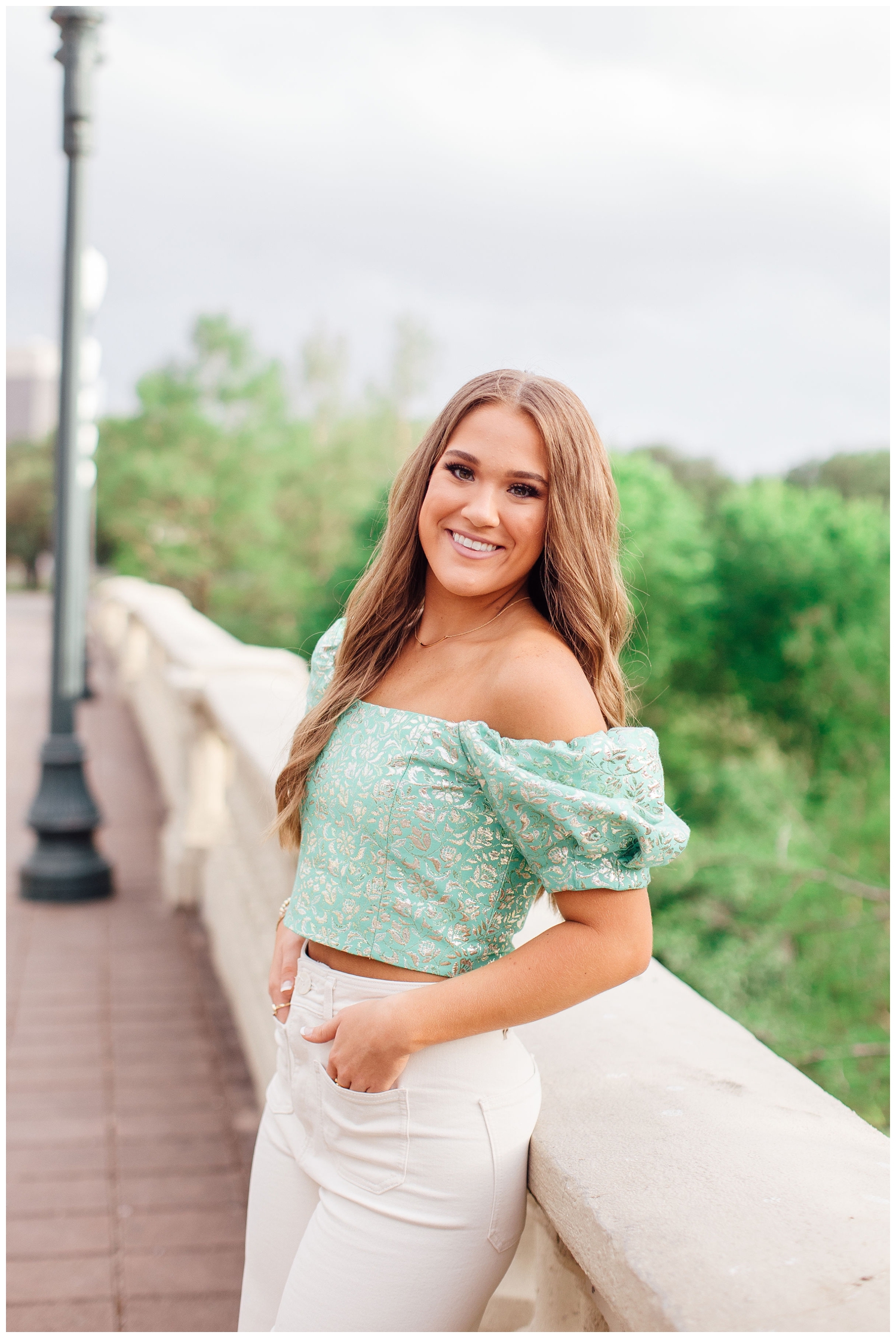 girl leaning on Sabine Street bridge for vibrant senior pictures in Houston in green blouse