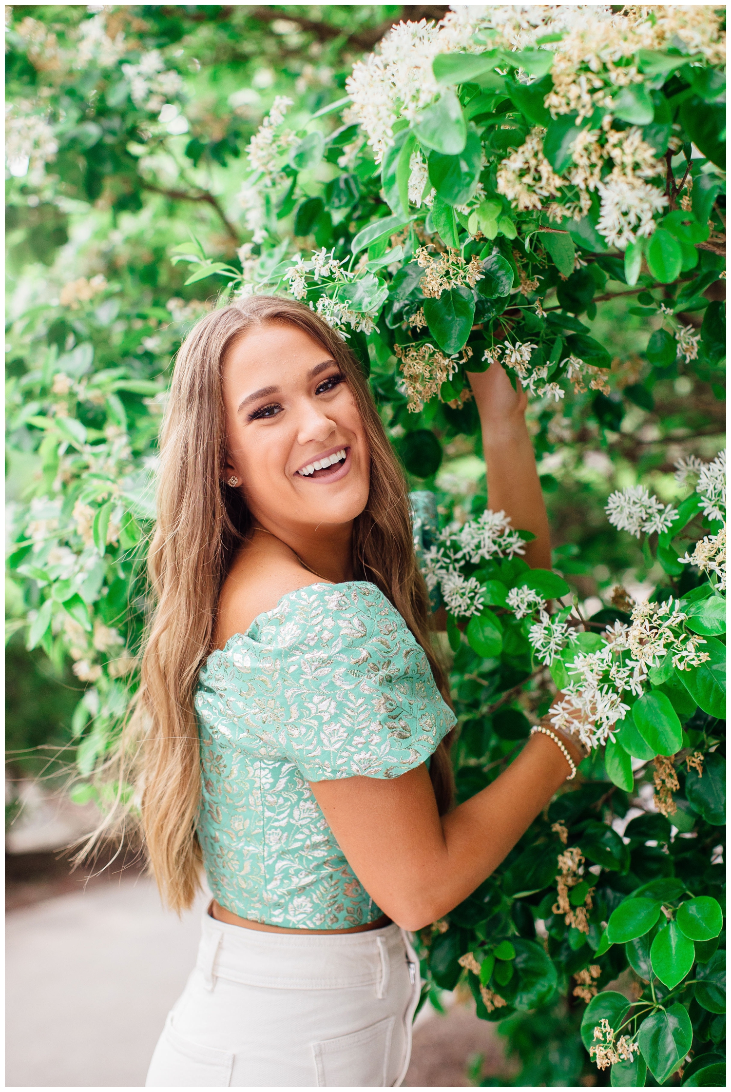 vibrant senior pictures in Houston of girl standing by a tree with flowers in a green shirt smiling