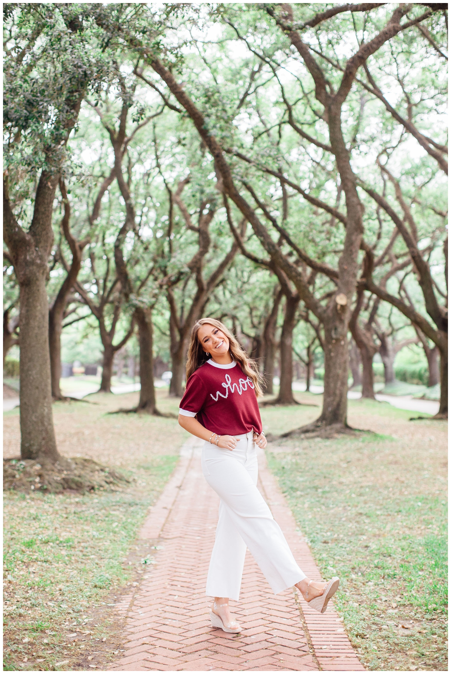 Vibrant senior pictures in Houston of girl in white shirt and maroon shirt standing in tree line