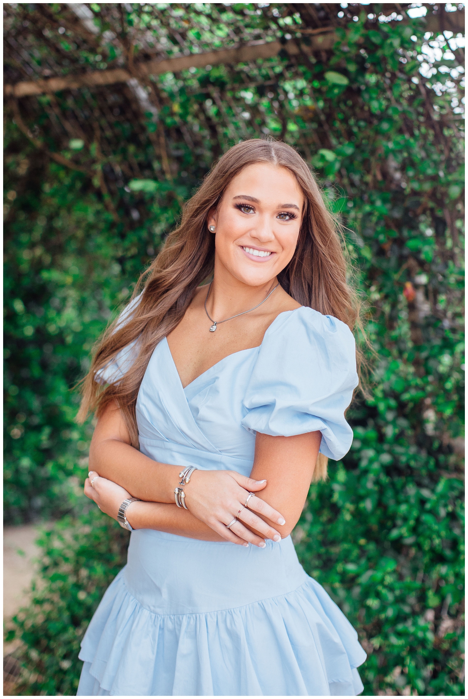 Vibrant senior pictures in Houston of girl wearing blue romper in front of green ivy wall