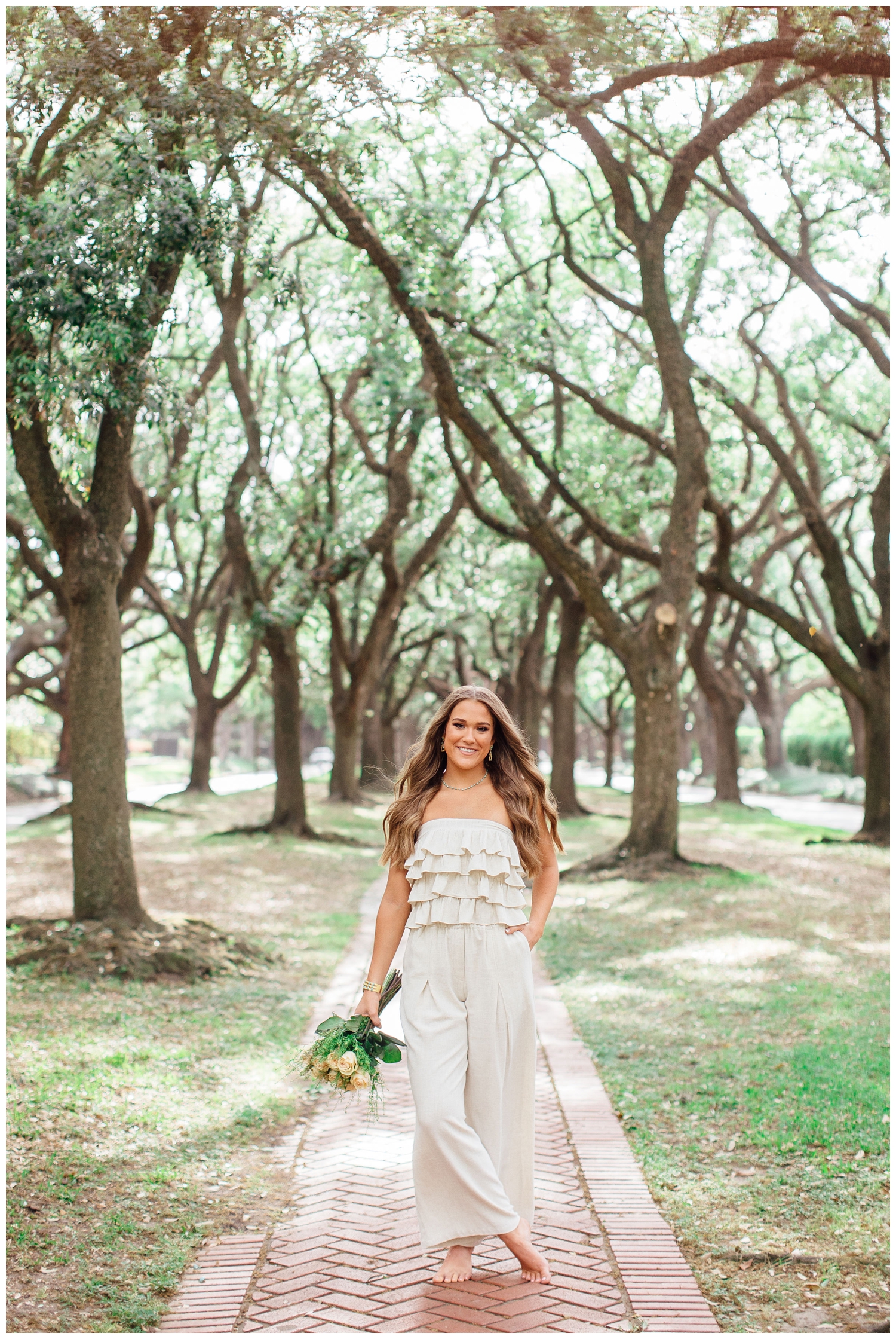 vibrant senior pictures in Houston with girl in white jumpsuit holding floral bouquet and walaking