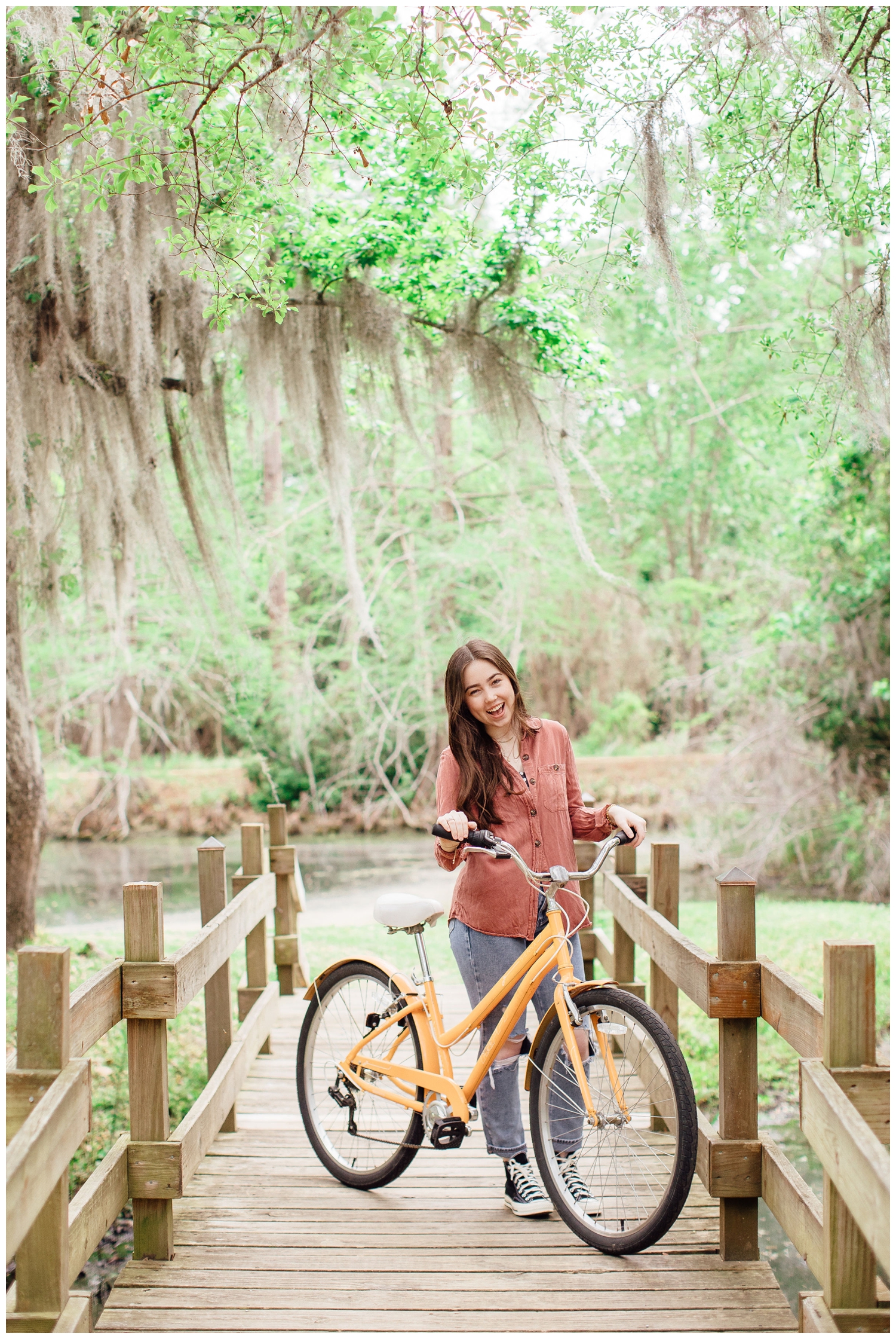 high school senior girl standing on mossy bridge at Cy-Hope holding yellow bike