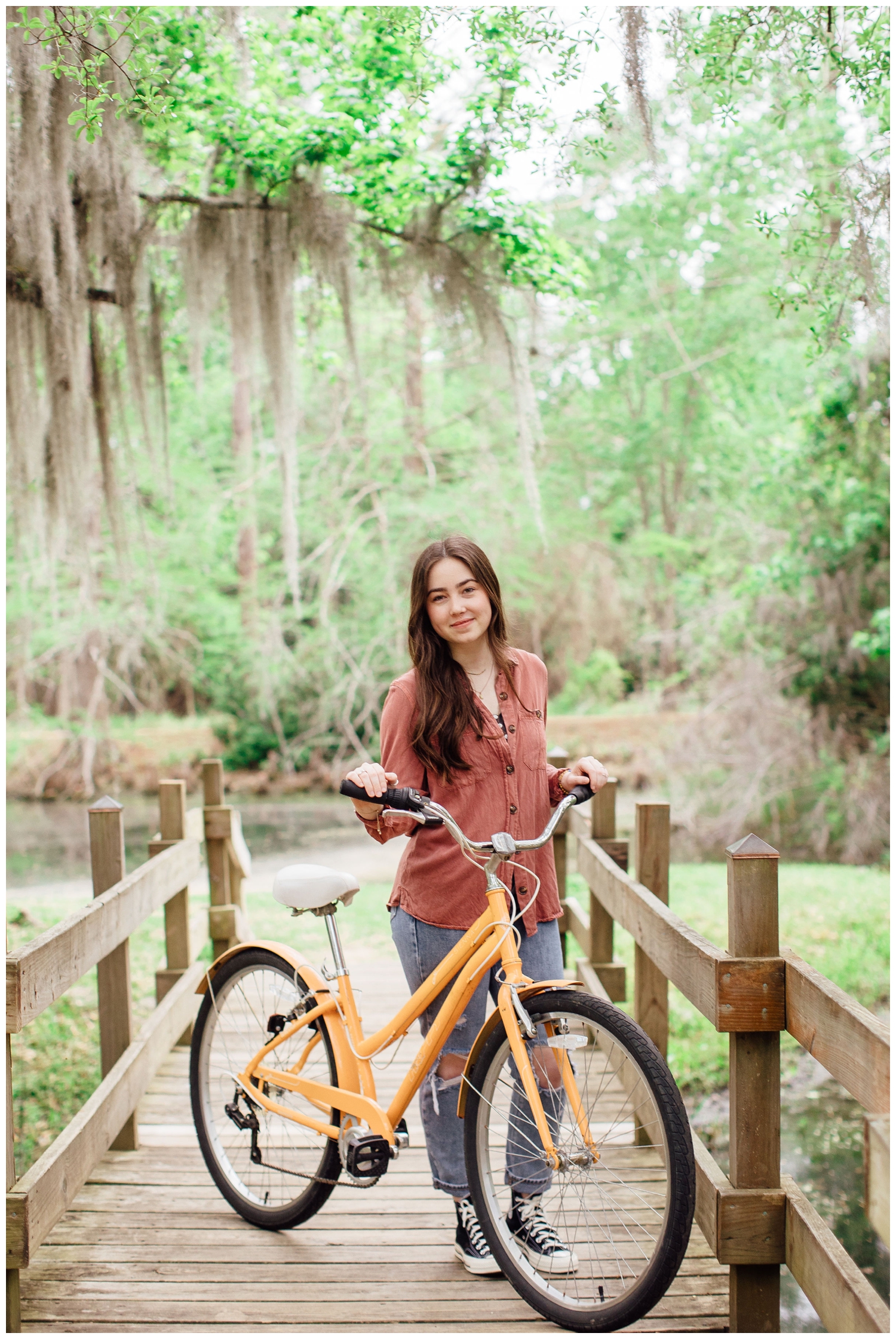 Cypress high school senior standing on mossy bridge holding a bike