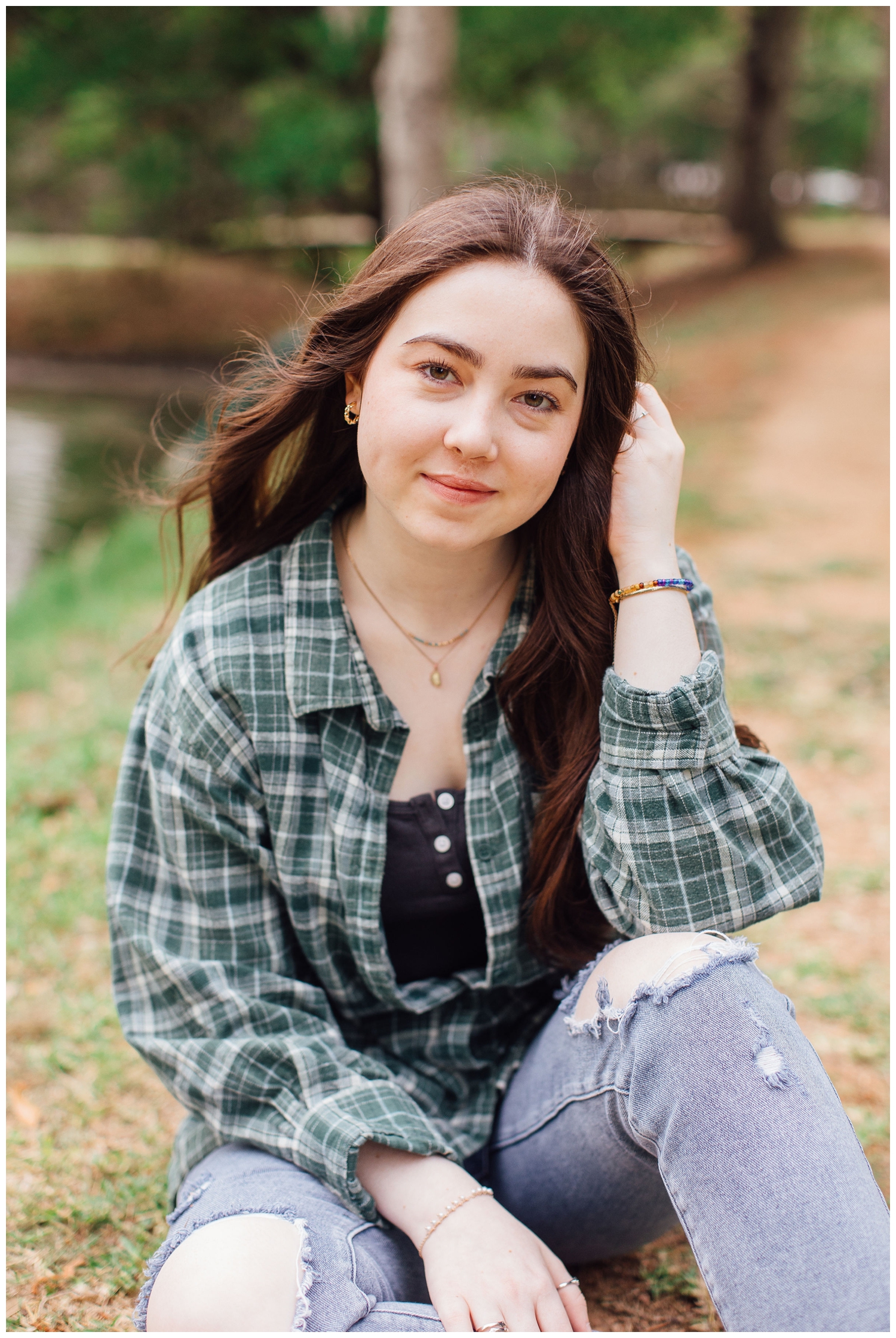girl sitting in field with hand in hair wearing plaid shirt and jeans