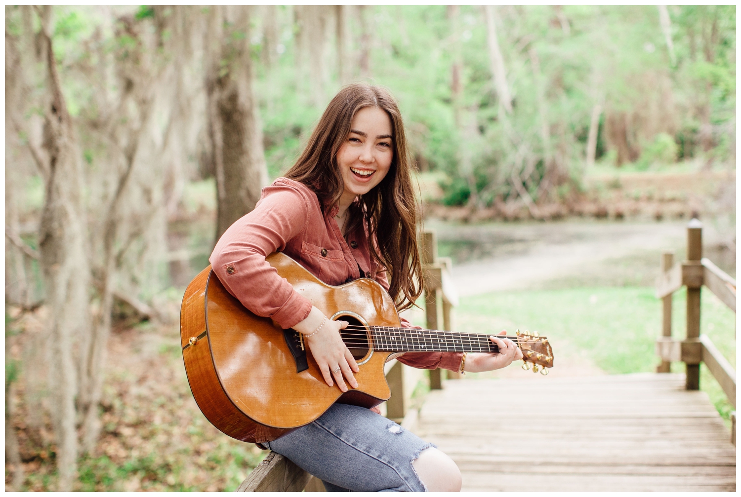 girl in jeans and rust colored shirt leaning on bridge Houston senior photos with guitar