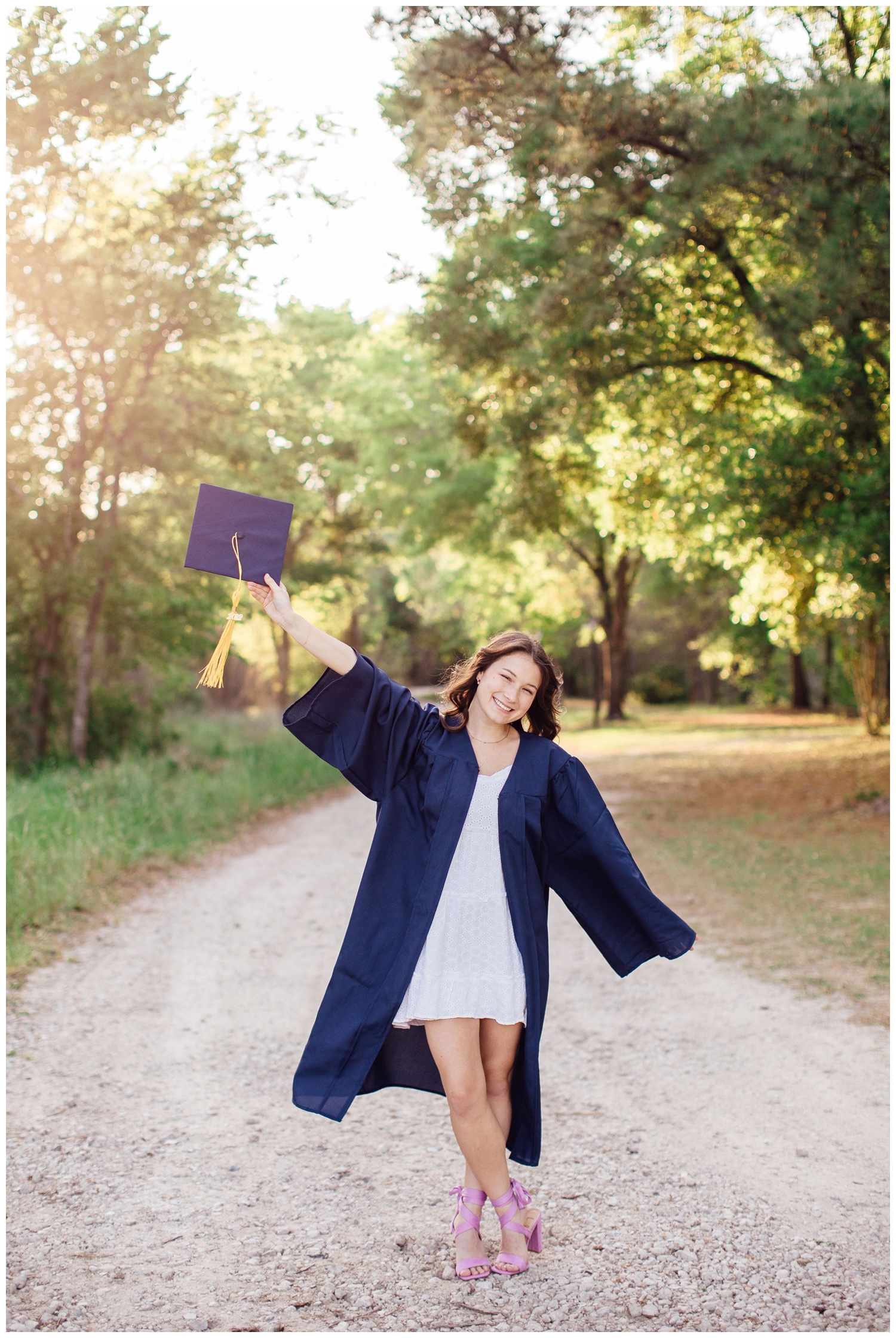 high school senior wearing cap and gown and standing on path way at Cy Hope for spring senior photos Houston