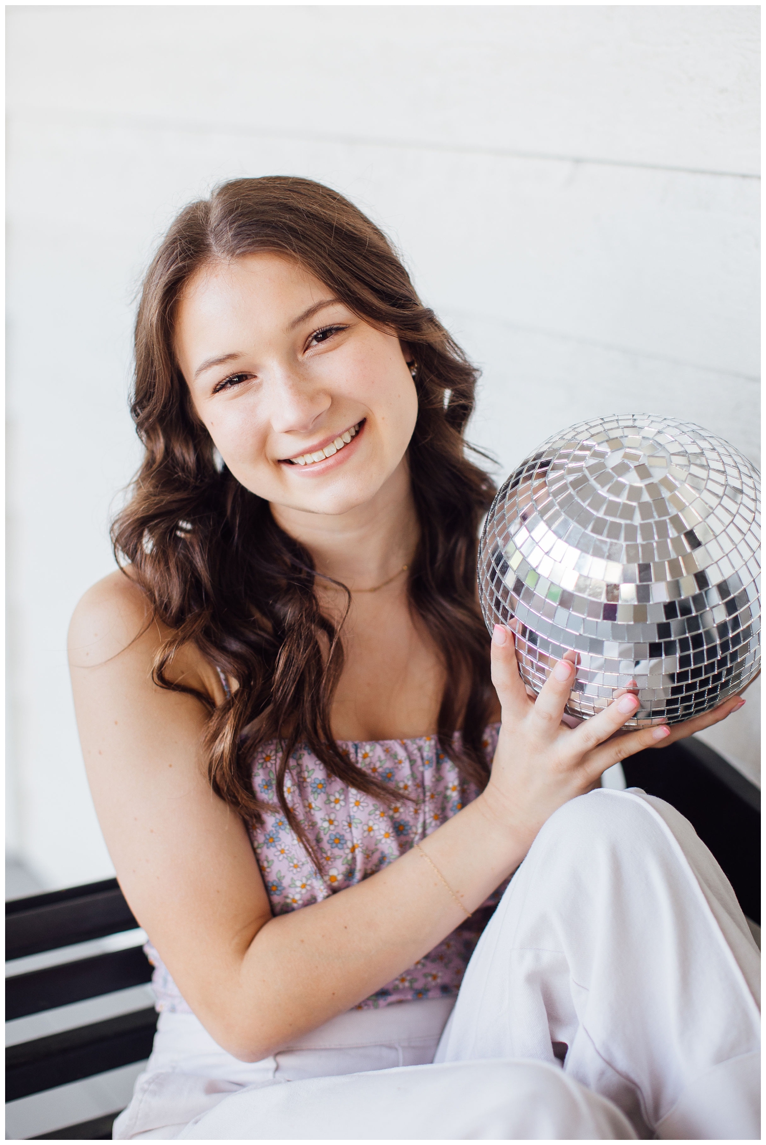 girl sitting on bench in white jeans holding silver disco ball