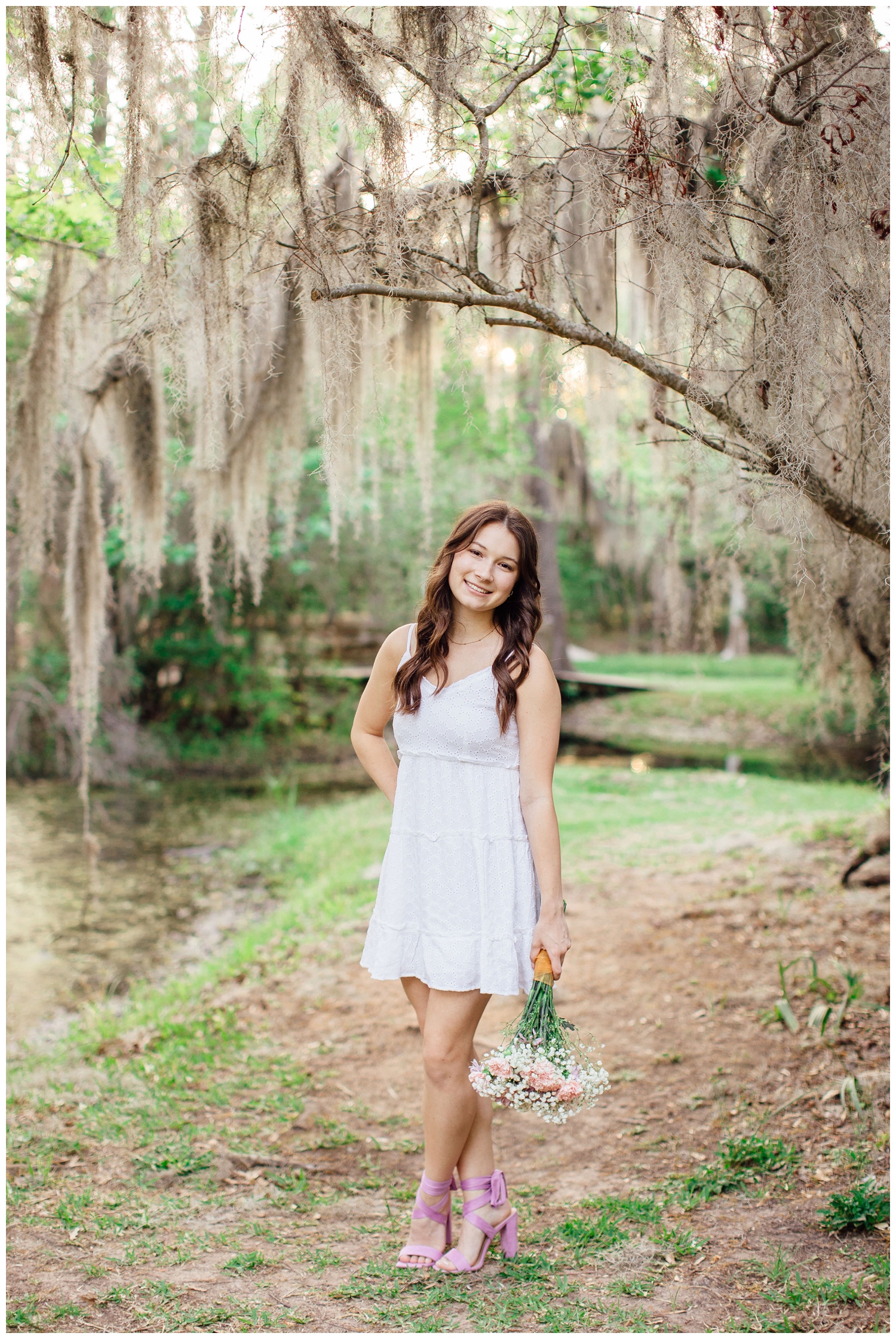 girl in white dress holding floral bouquet by her side standing under moss tree Houston Texas