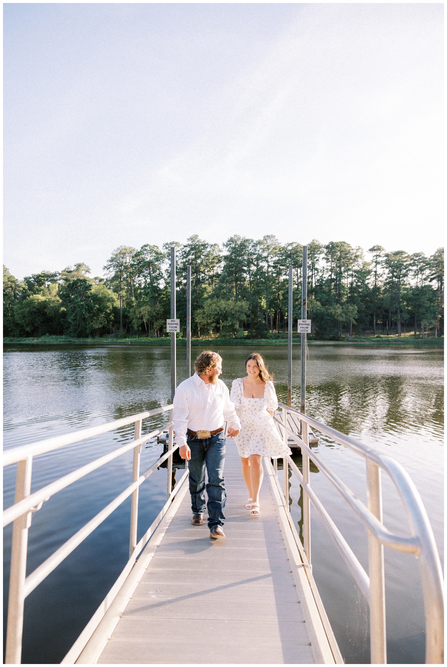 couple holding hands and walking on a boat dock in front of a lake