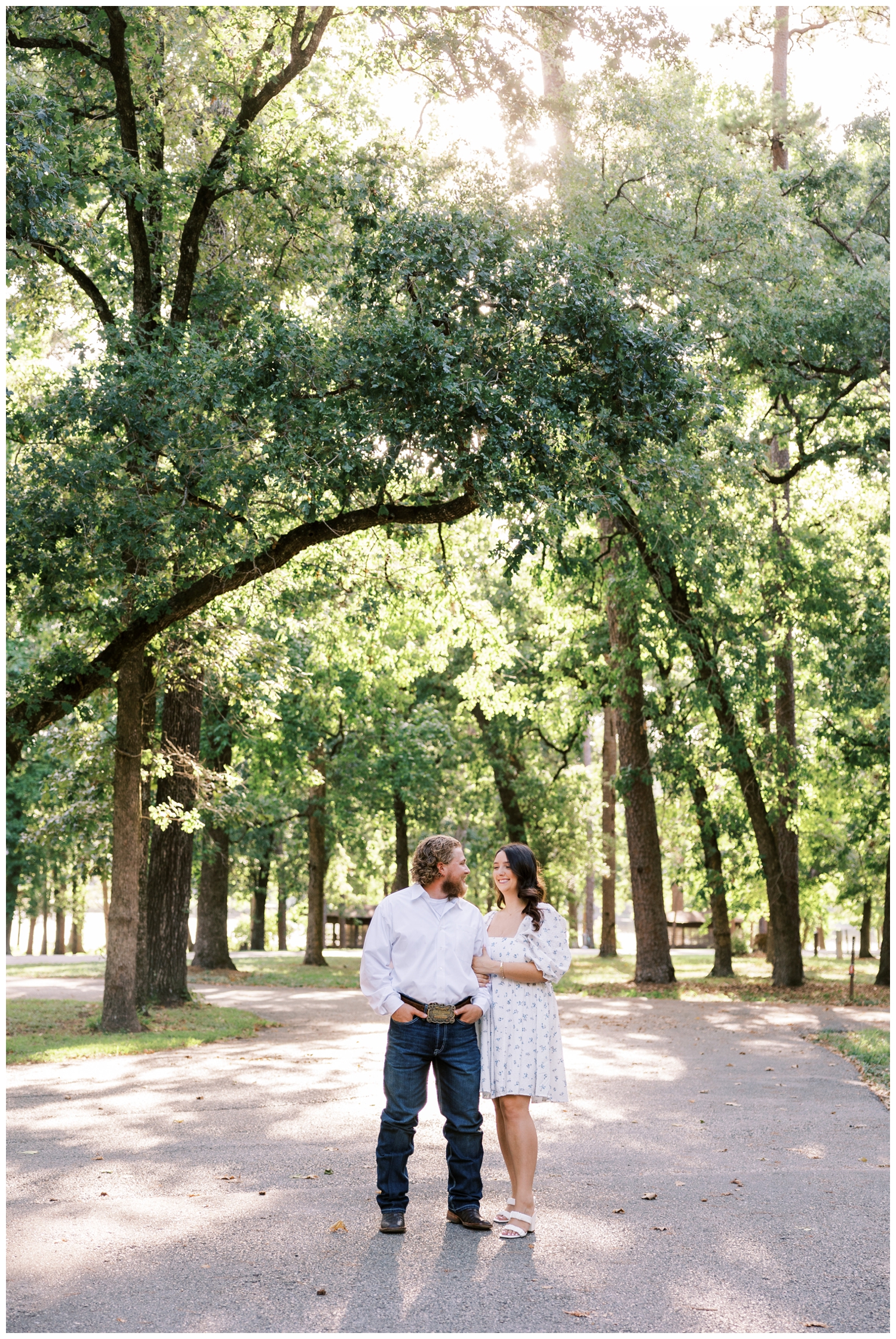 couple in white smiling at each other under trees at a texas park