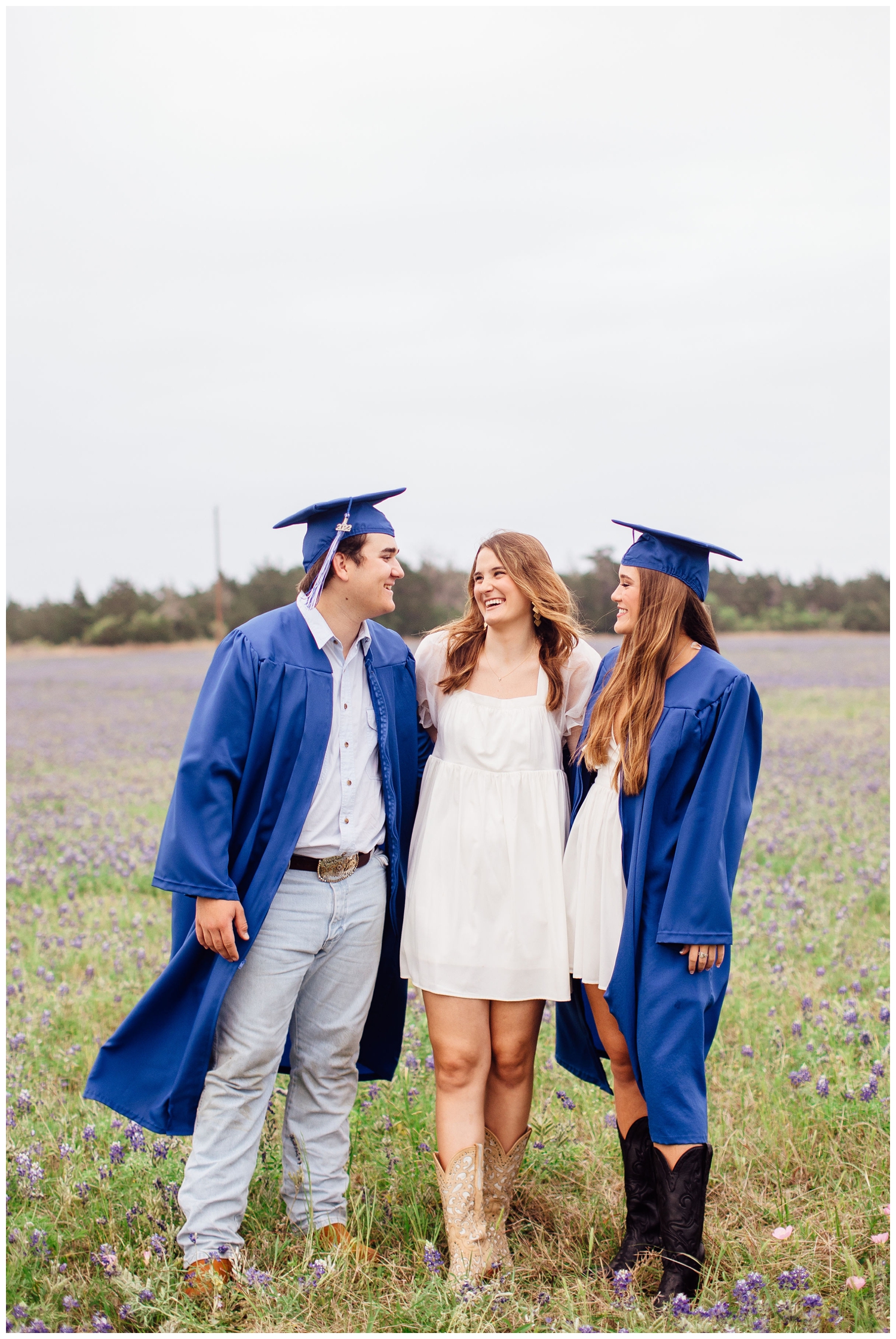 sisters and brother in cap and gown photo laughing in bluebonnet field