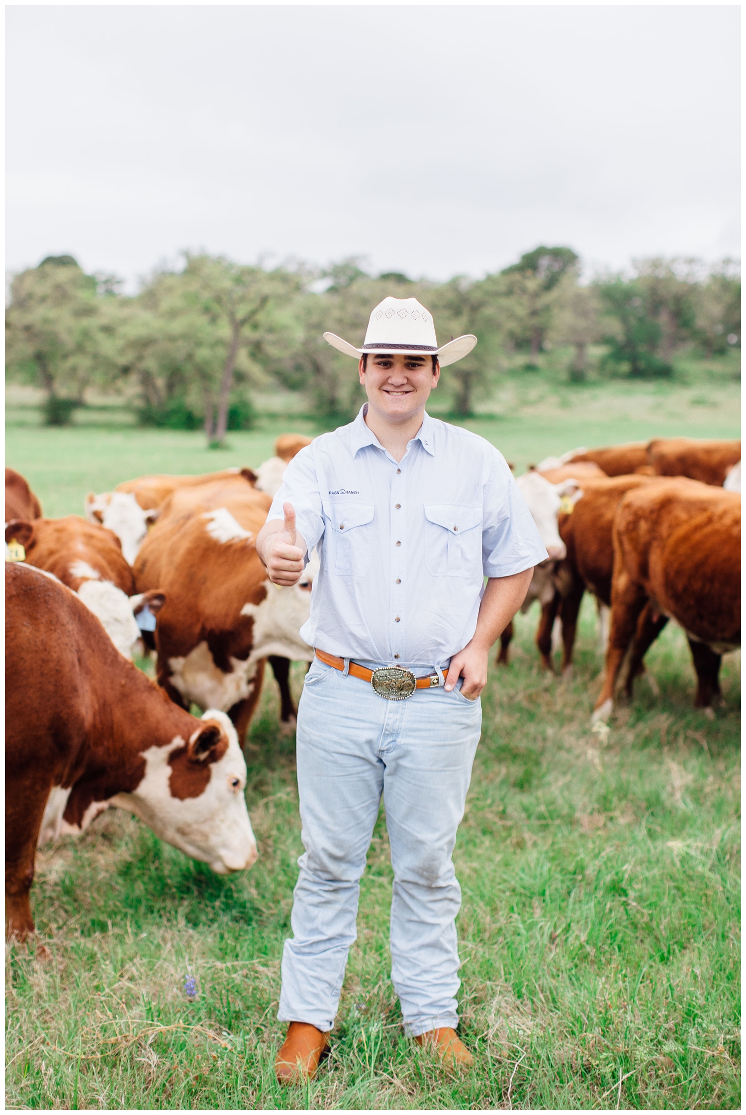 guy in jeans and cowboy hat standing in middle of cows for senior pictures for guys session outside Houston, Texas