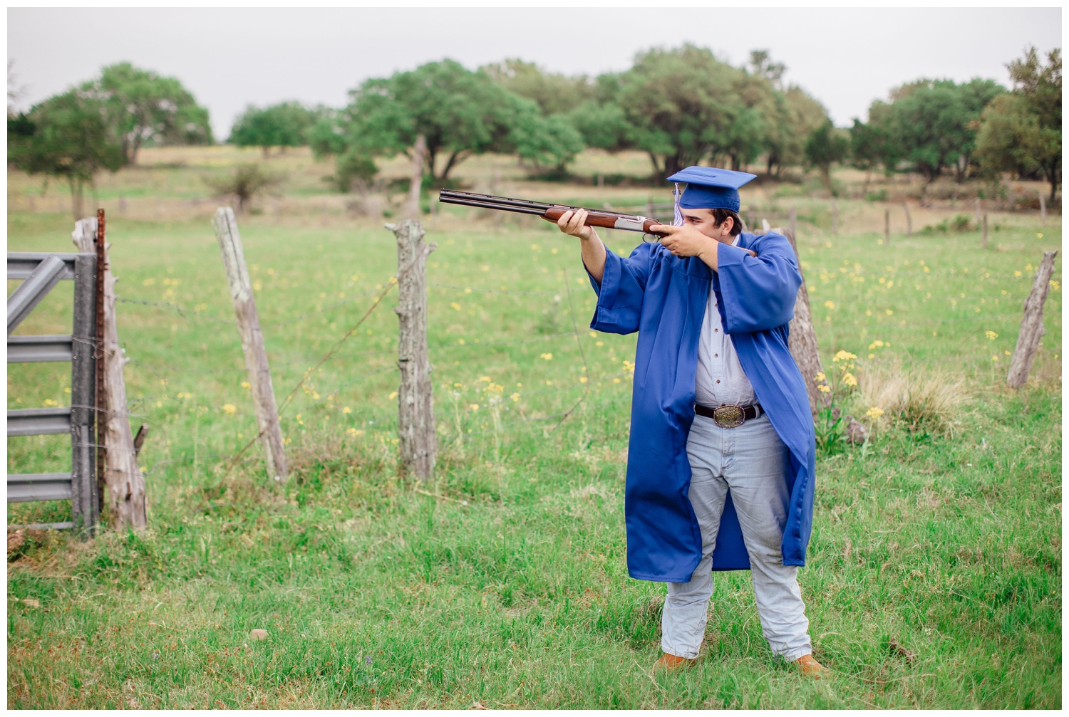 Houston high school senior guy wearing cap and gown standing in a field with a rifle