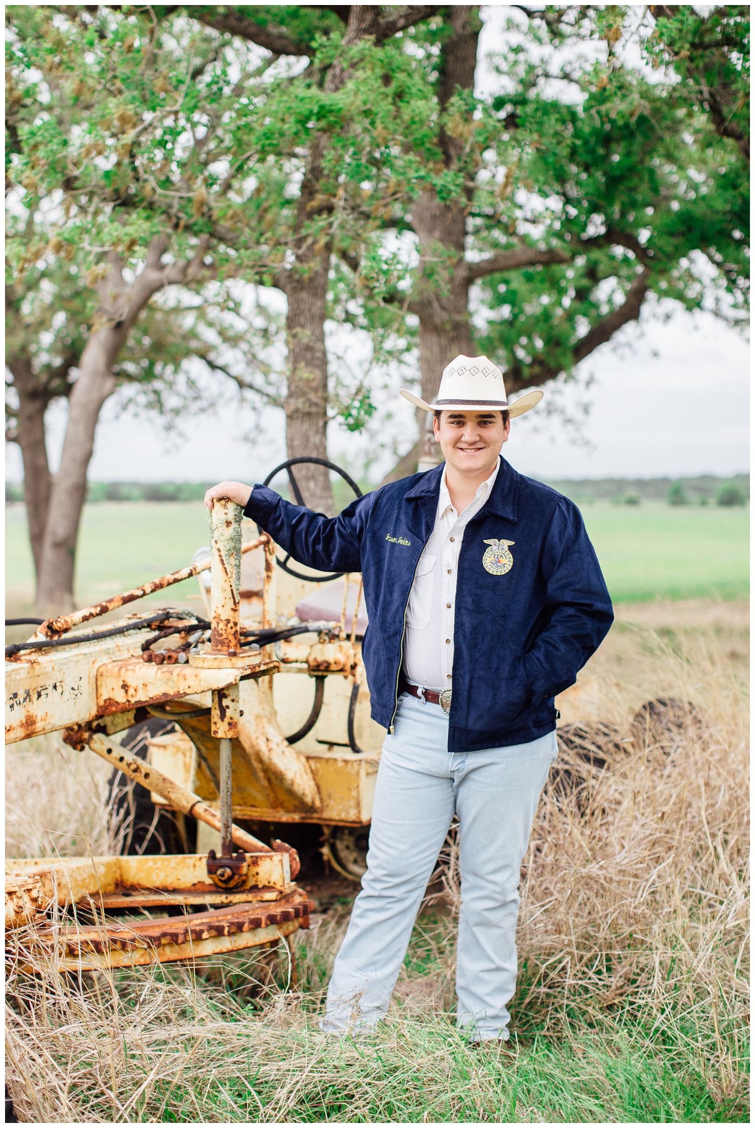 Senior Pictures for Guys at ranch outside Houston, Texas with guy holding onto a tractor in jeans and cowboy hat