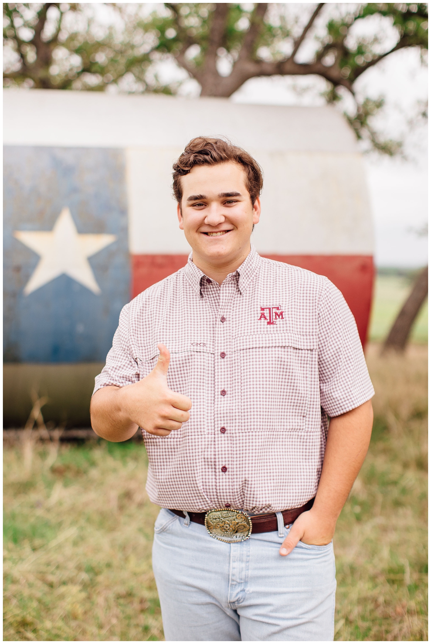 high school senior guy smiling at camera in plaid shirt and jeans with Gig Em hand sign
