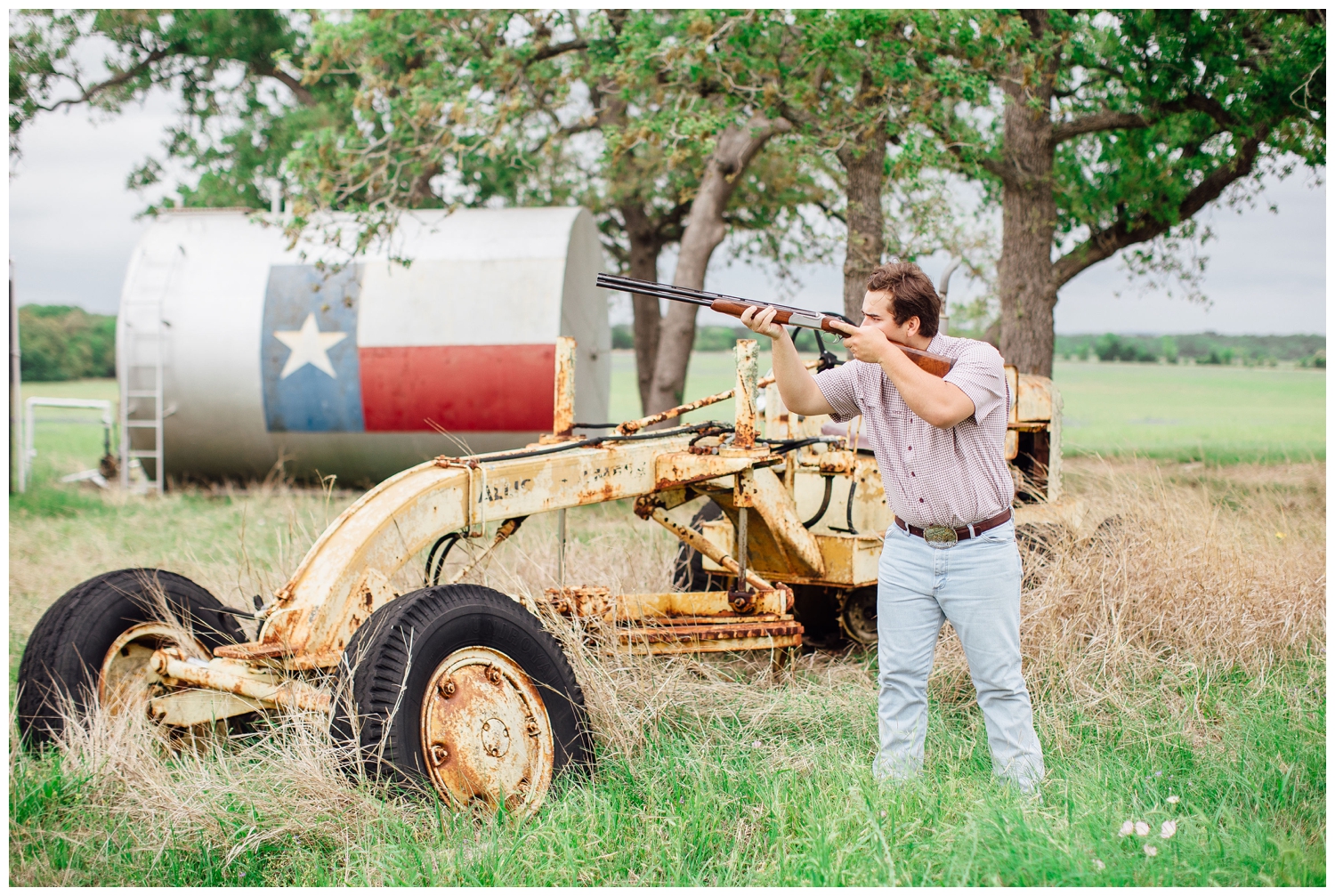 guy pointing a rifle in front of tractor for senior pictures for guys Houston, Texas