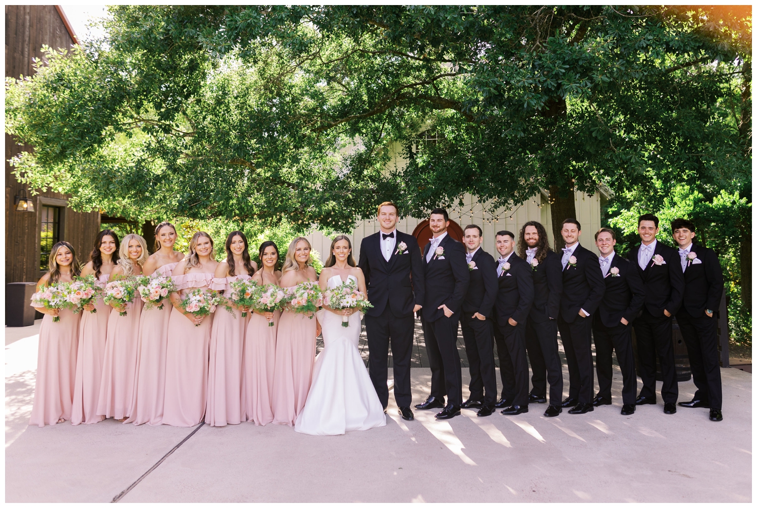 full wedding party standing under tree at The Carriage House Houston wedding venue