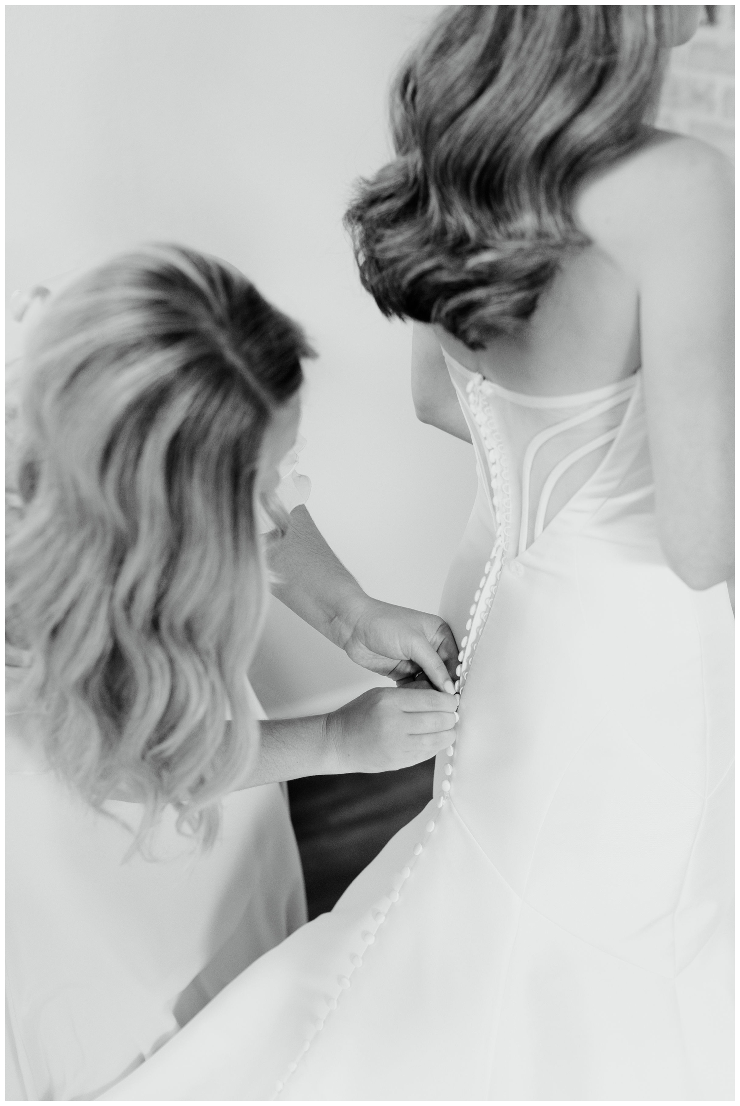 black and white portrait of mom fastening brides wedding gown