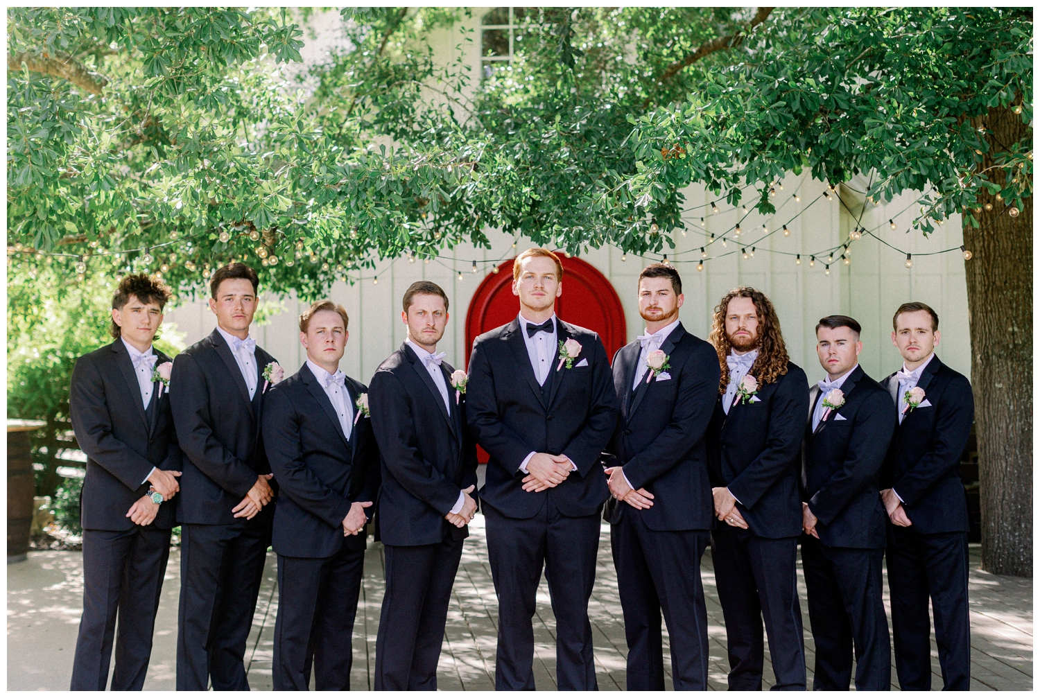 groom and groomsmen standing in a line in front of red door at The Carriage House Houston