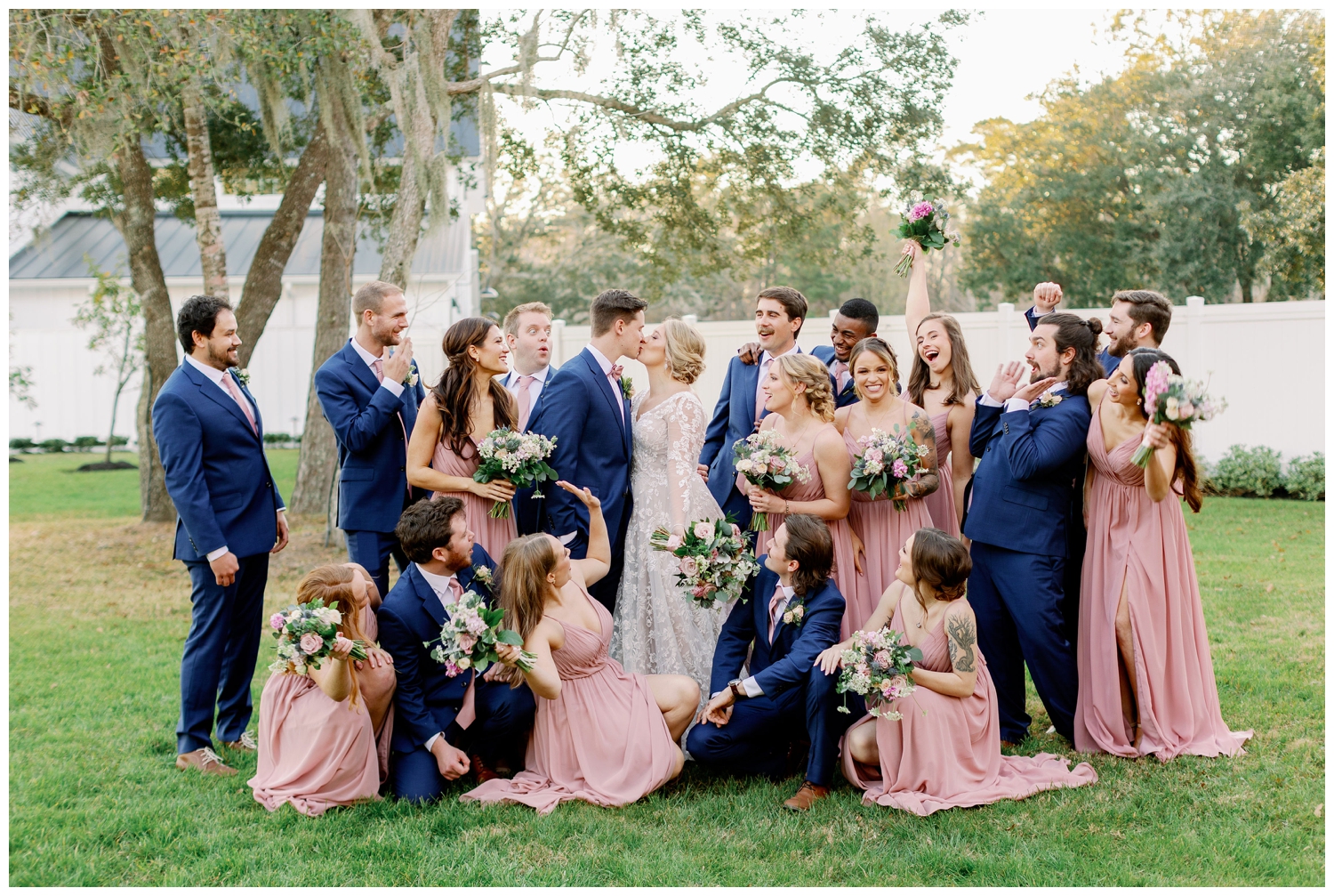bride and groom kissing surrounded by their wedding party under trees at The Springs Wallisville Wedding venue
