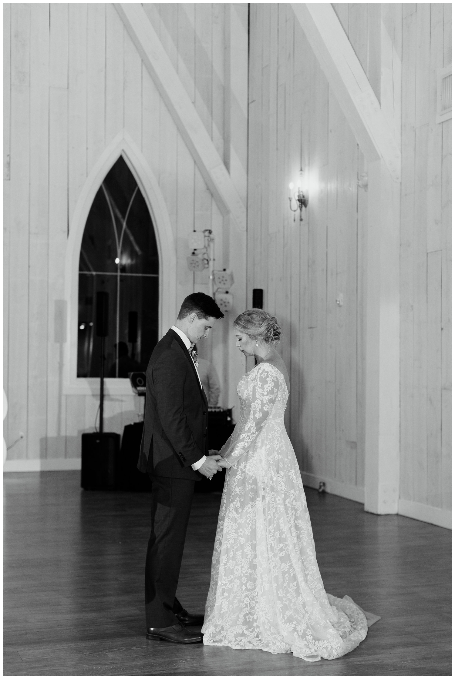 black and white image of bride and groom holding hands and praying during reception