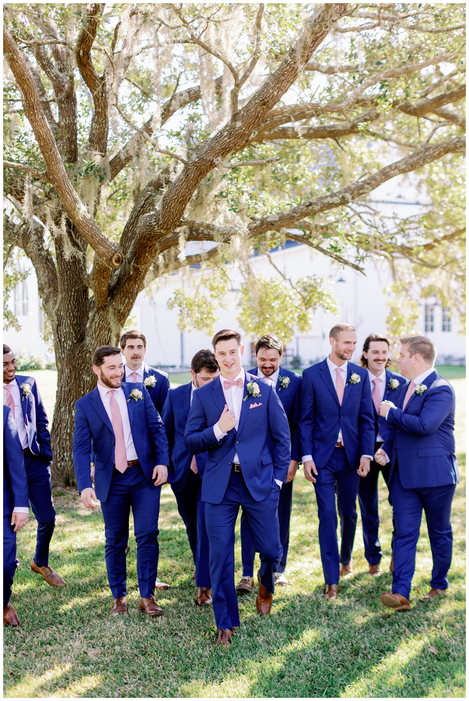 groom and groomsmen in blue suits and pink tie walking outside The Springs Wallisville Wedding venue for portraits