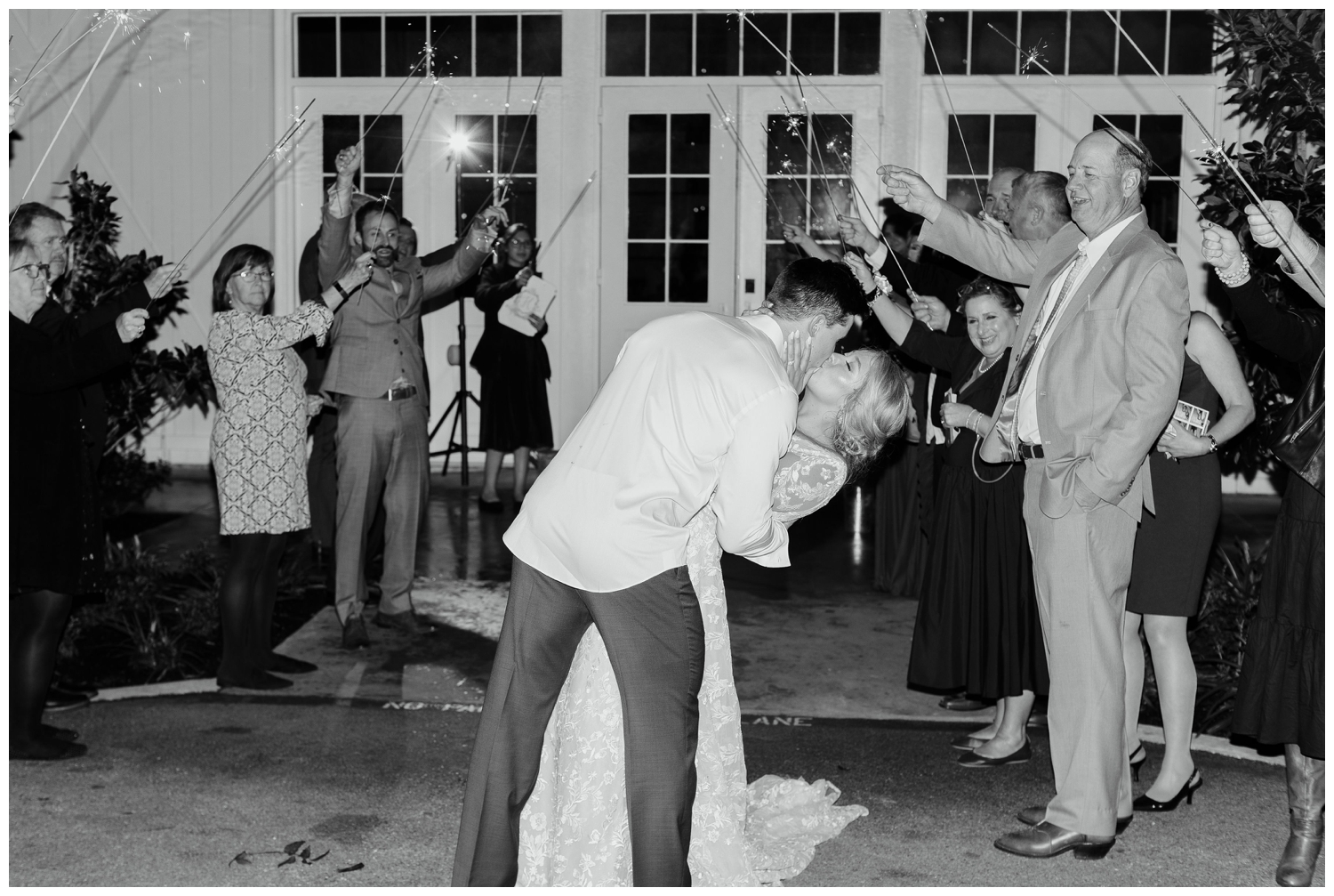black and white image of bride and groom dipping and kissing during sparkler exit