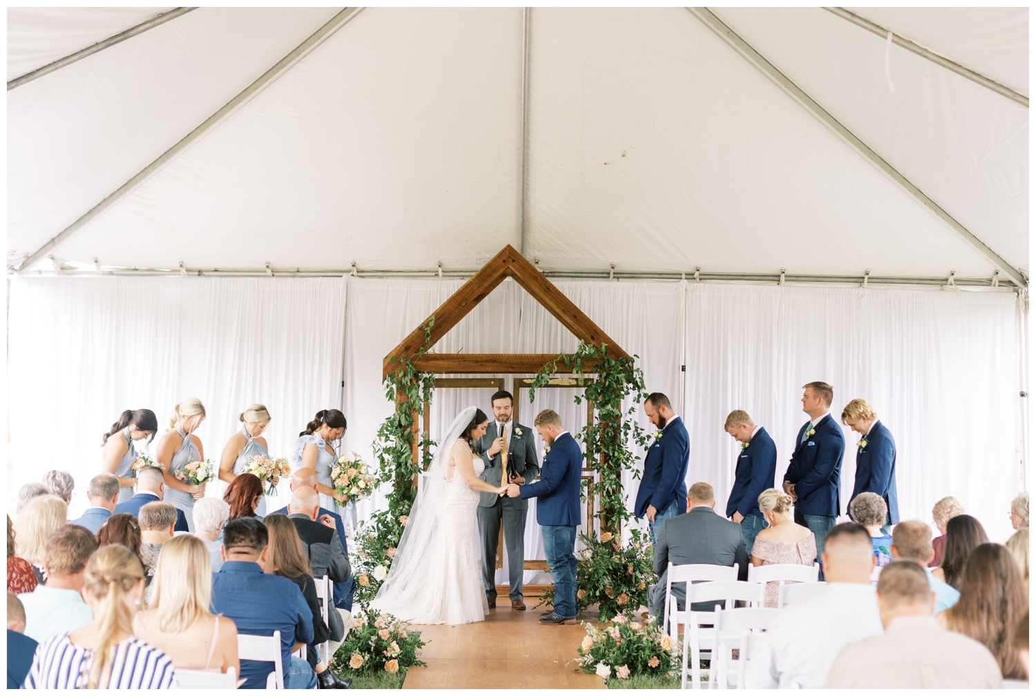 bride and groom holding hands praying outdoor tent ceremony