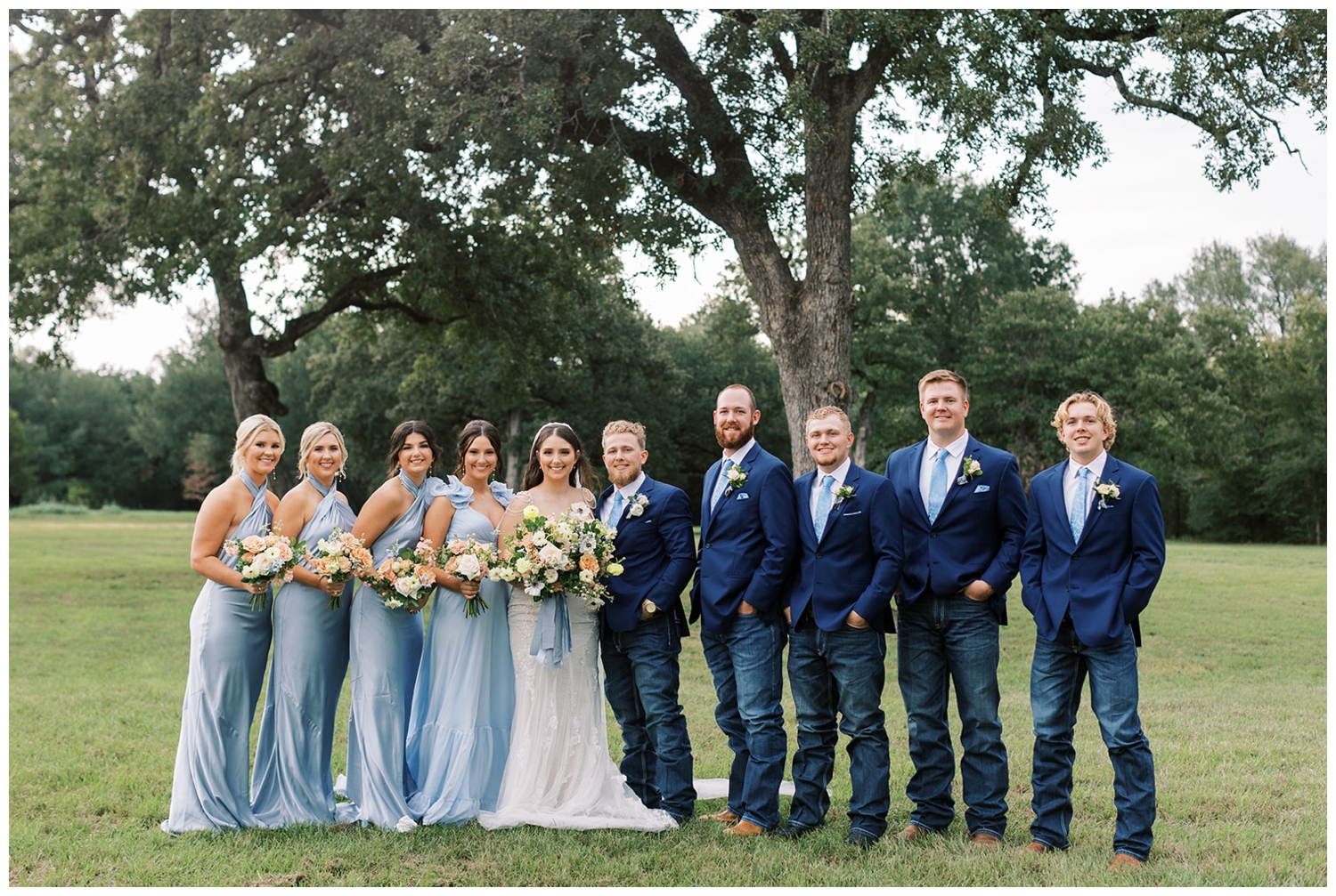 full wedding party in blue with bride and groom standing in middle outside at Bluebird Haven Estates Wedding venue