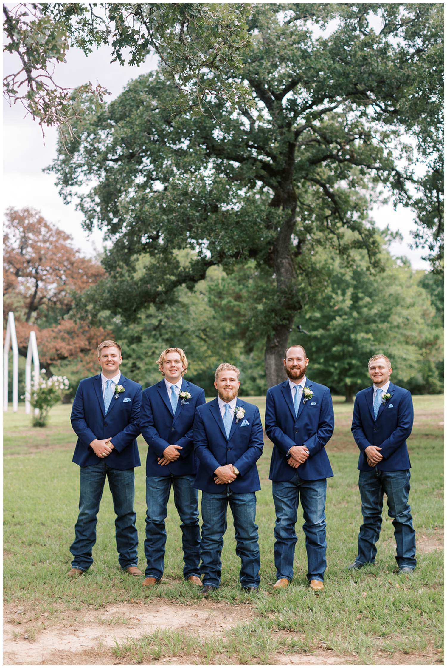 groom and groomsmen in blue suits standing outside under a tree in Madisonville Texas