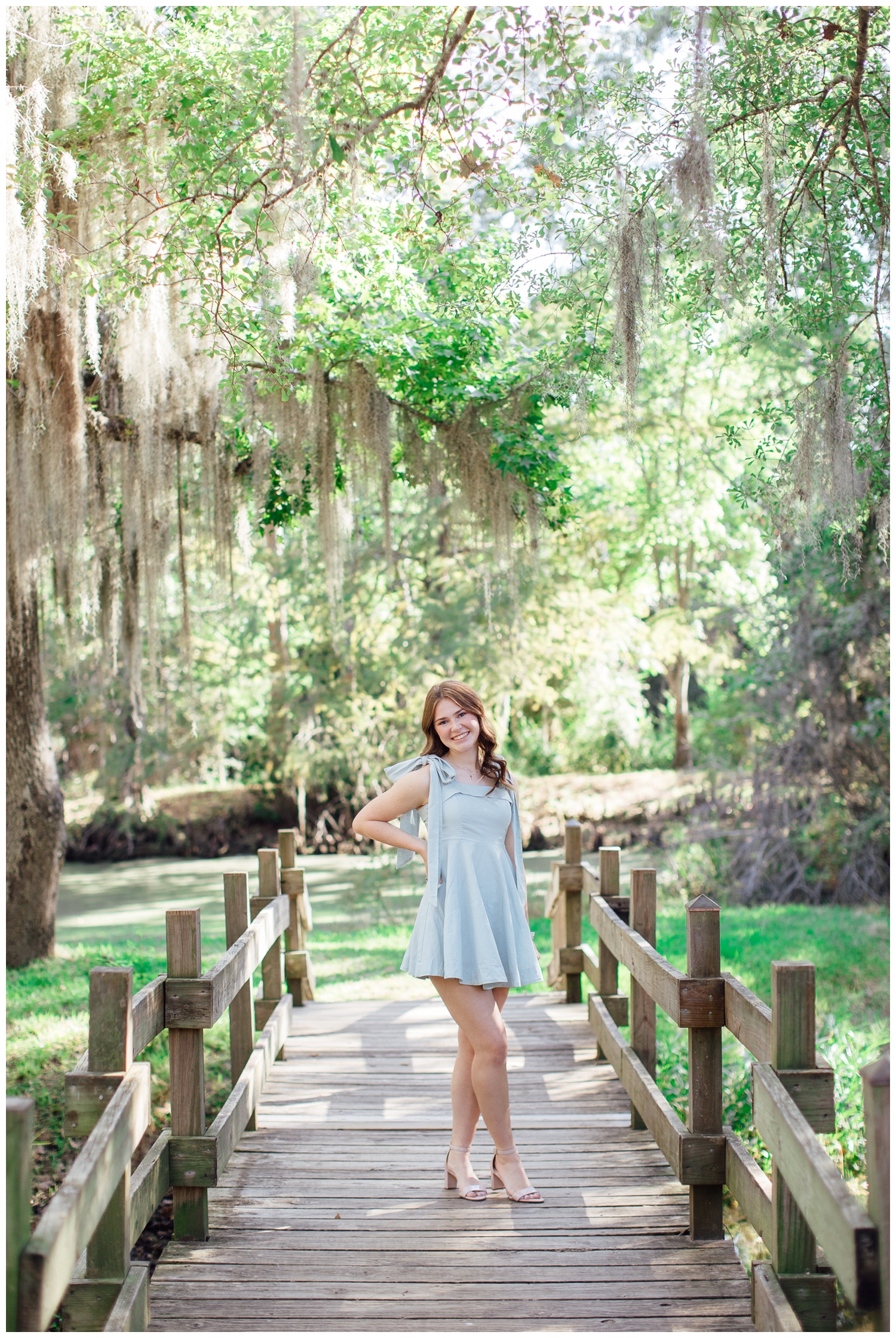 Fall senior photos Houston with girl in blue dress standing on bridge under mossy trees