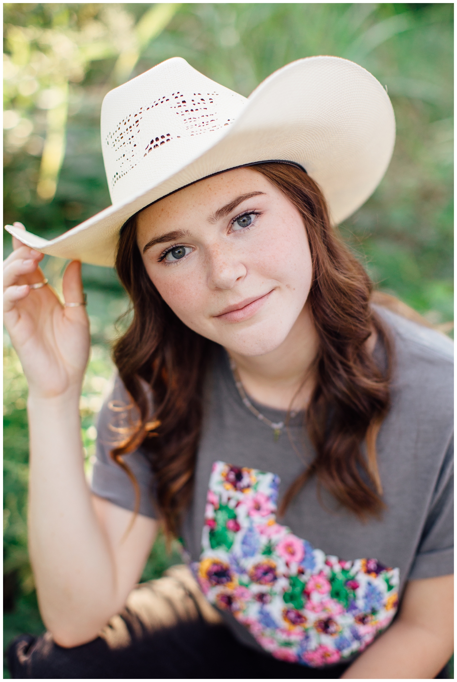 girl sitting with hand on cowboy hat for fall senior photos Houston outdoors