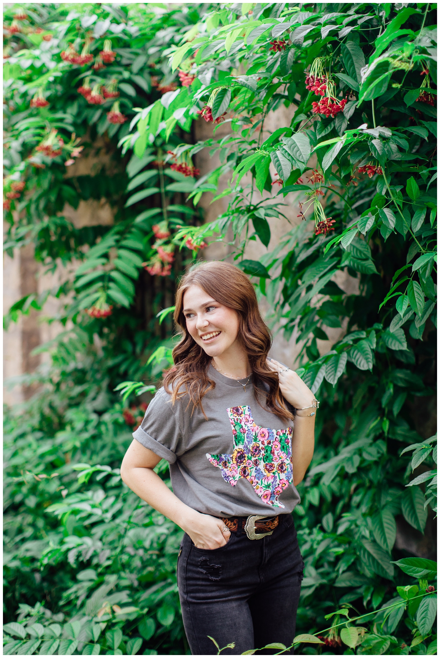 high school senior girl laughing over her shoulder standing in front of green vines outdoors for fall senior photos Houston