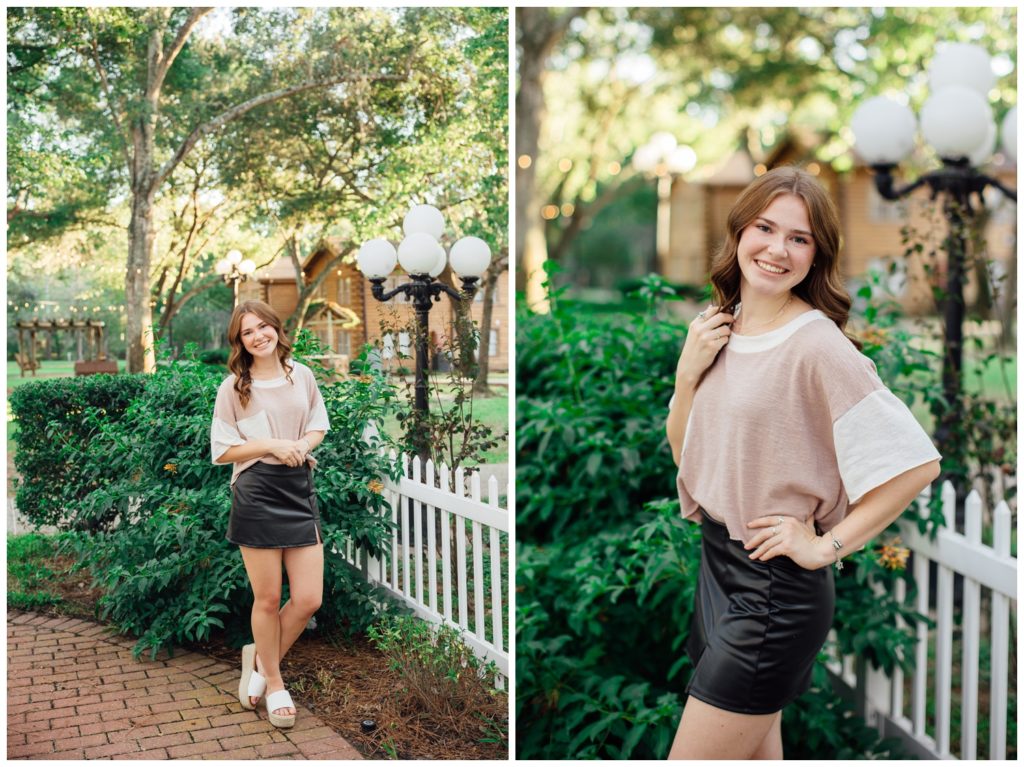 girl in black skirt and cream sweater leaning against white picket fence for fall senior photos Houston and smiling outdoors