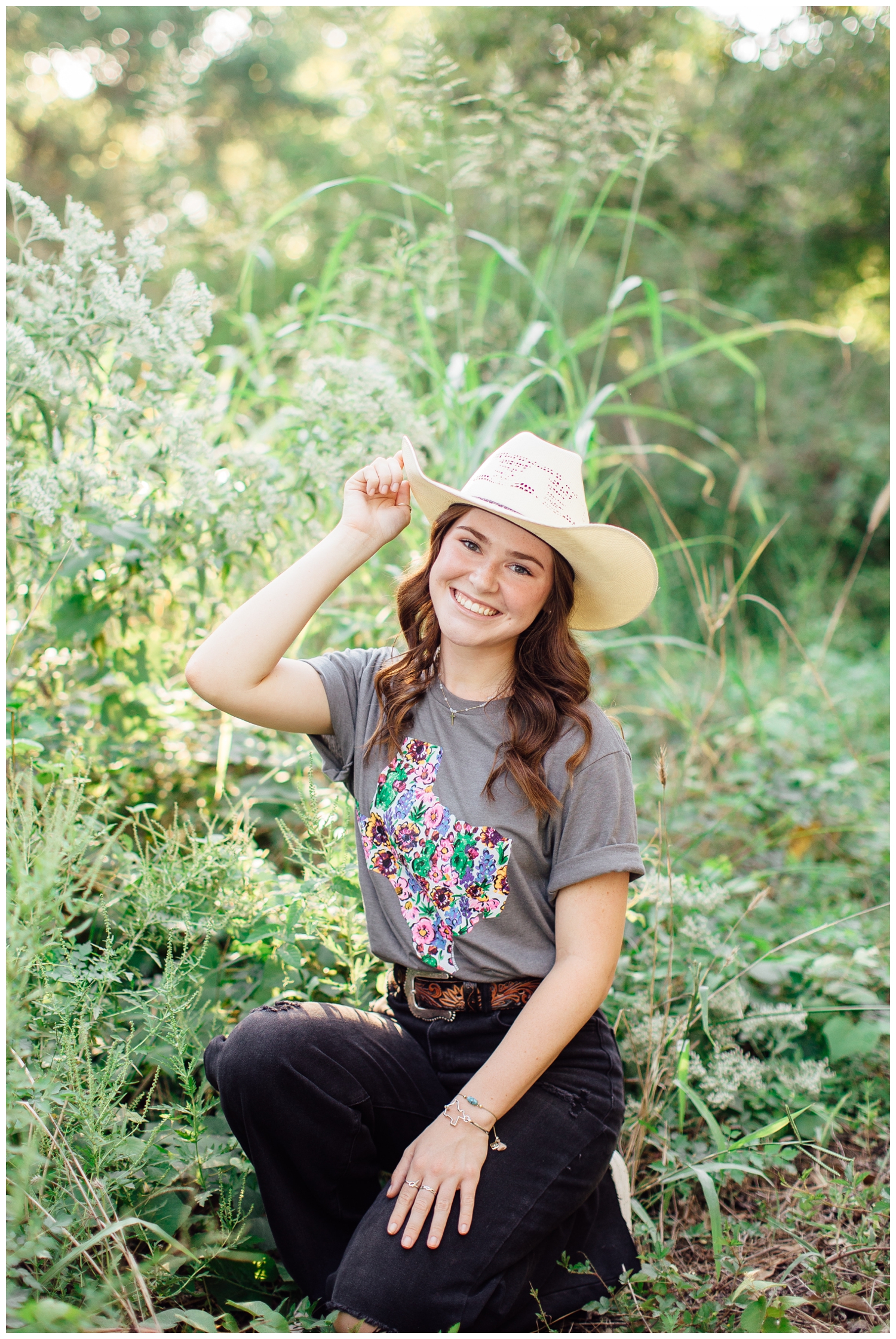 high school senior girl sitting outdoors in a field tipping her cowboy hat